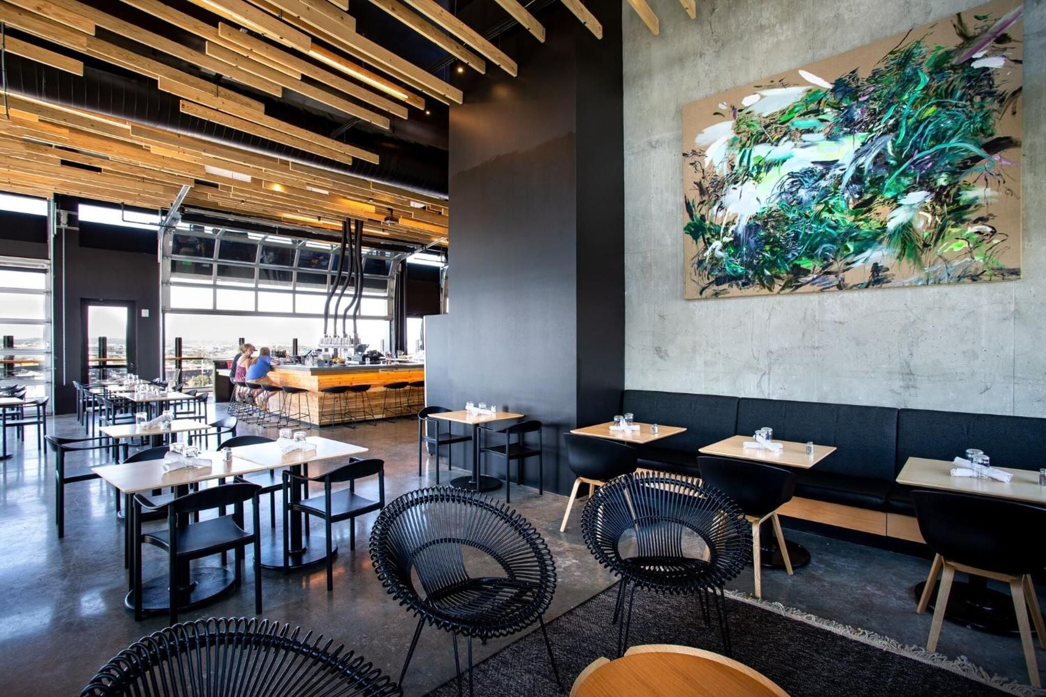 Exposed wooden beams and concrete walls create an industrial-chic backdrop where vibrant artwork pops against the neutral palette of this contemporary dining space.