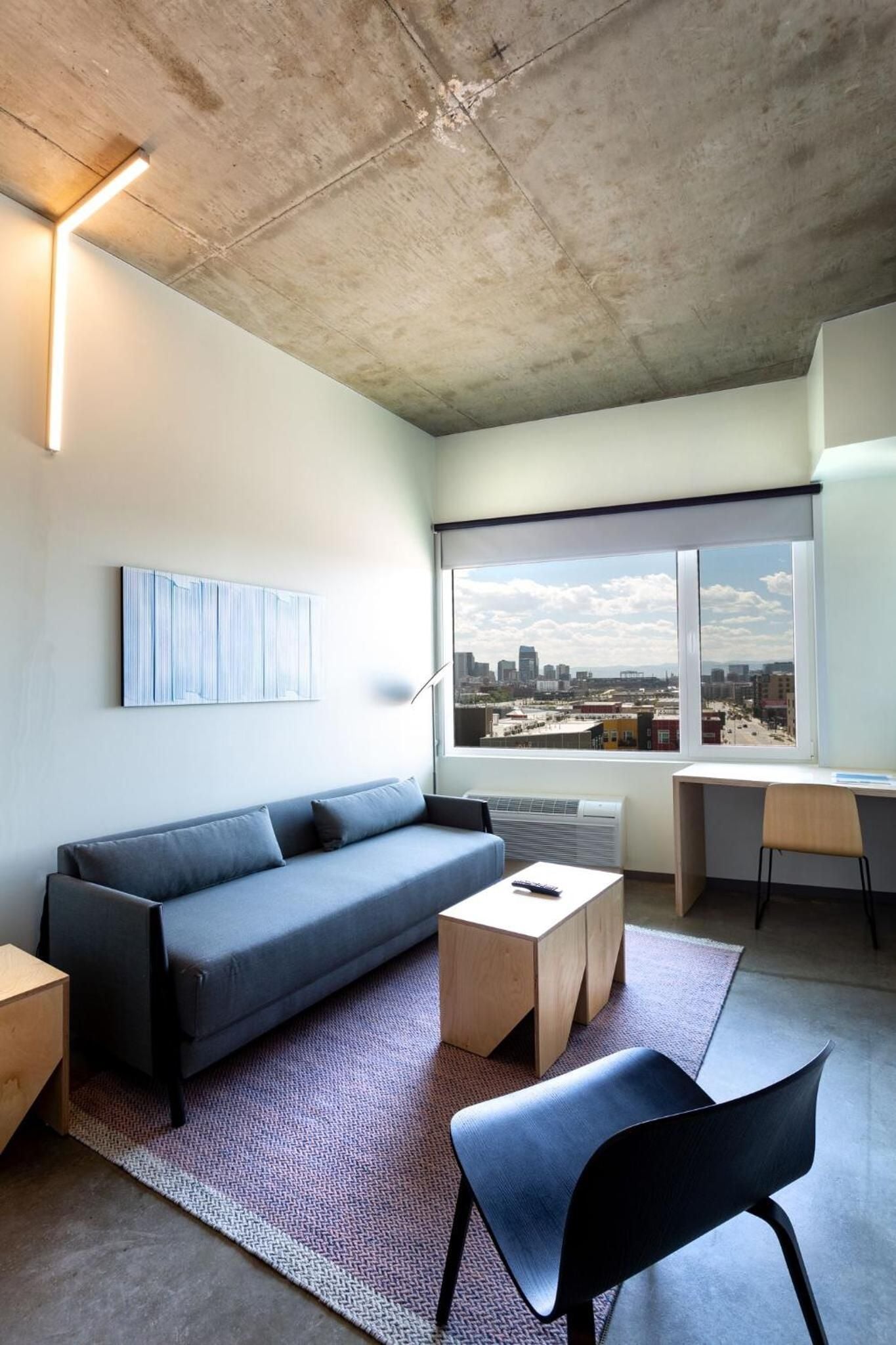 Raw concrete ceilings contrast beautifully with warm wood furnishings in this thoughtfully appointed suite, where floor-to-ceiling windows frame downtown Denver's evolving skyline.