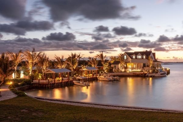 Golden hour bathes Abaco Inn's waterfront buildings in warm light as palm trees sway above the tranquil harbor, where gentle waves lap against the sandy shore.