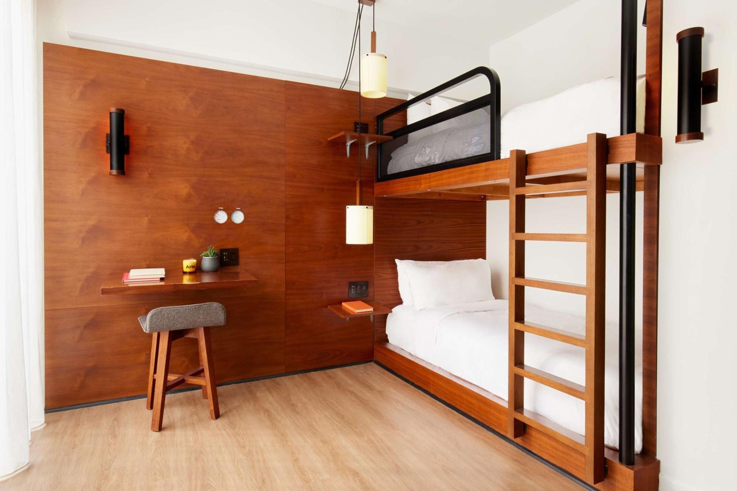 Warm walnut paneling and industrial-chic bunk beds maximize every inch of this thoughtfully designed micro room, where pendant lighting creates intimate pockets of warmth.