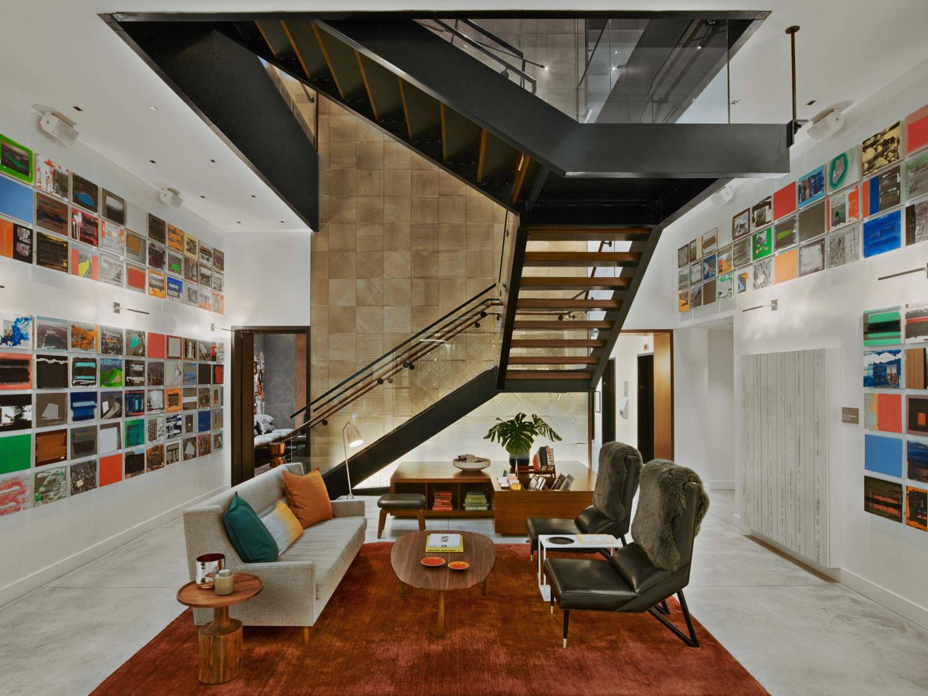 Record album covers create a vibrant gallery wall in this double-height lounge, where mid-century furniture and dramatic angular stairs foster creative conversations beneath soaring ceilings.