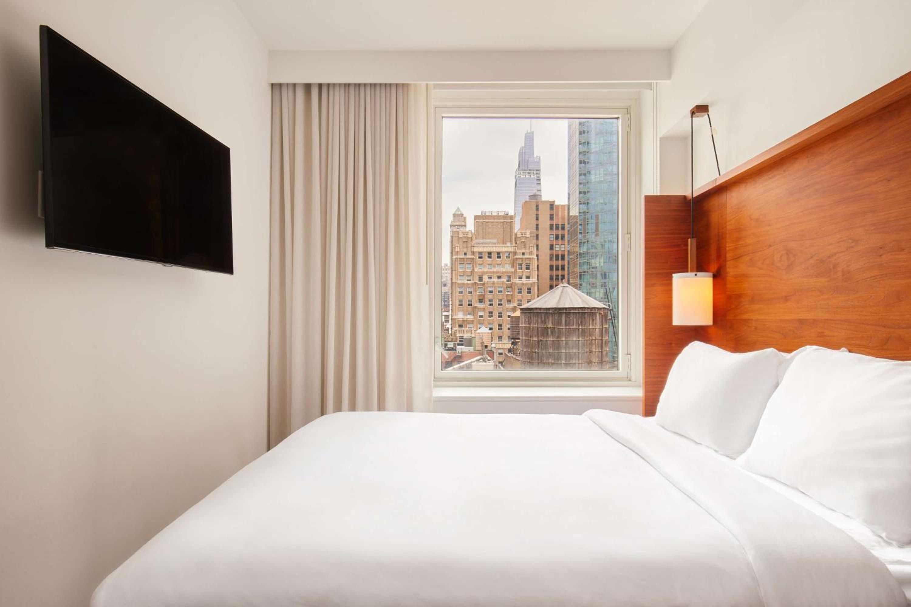 Floor-to-ceiling windows frame Manhattan's iconic water tower and brick facades from this crisp, wood-accented room where city energy meets serene minimalism.