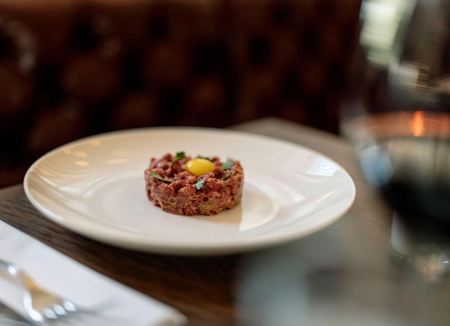 Hand-cut steak tartare arrives artfully molded with quail egg and fresh herbs, embodying ROOST's commitment to elevated comfort dining in intimate surroundings.
