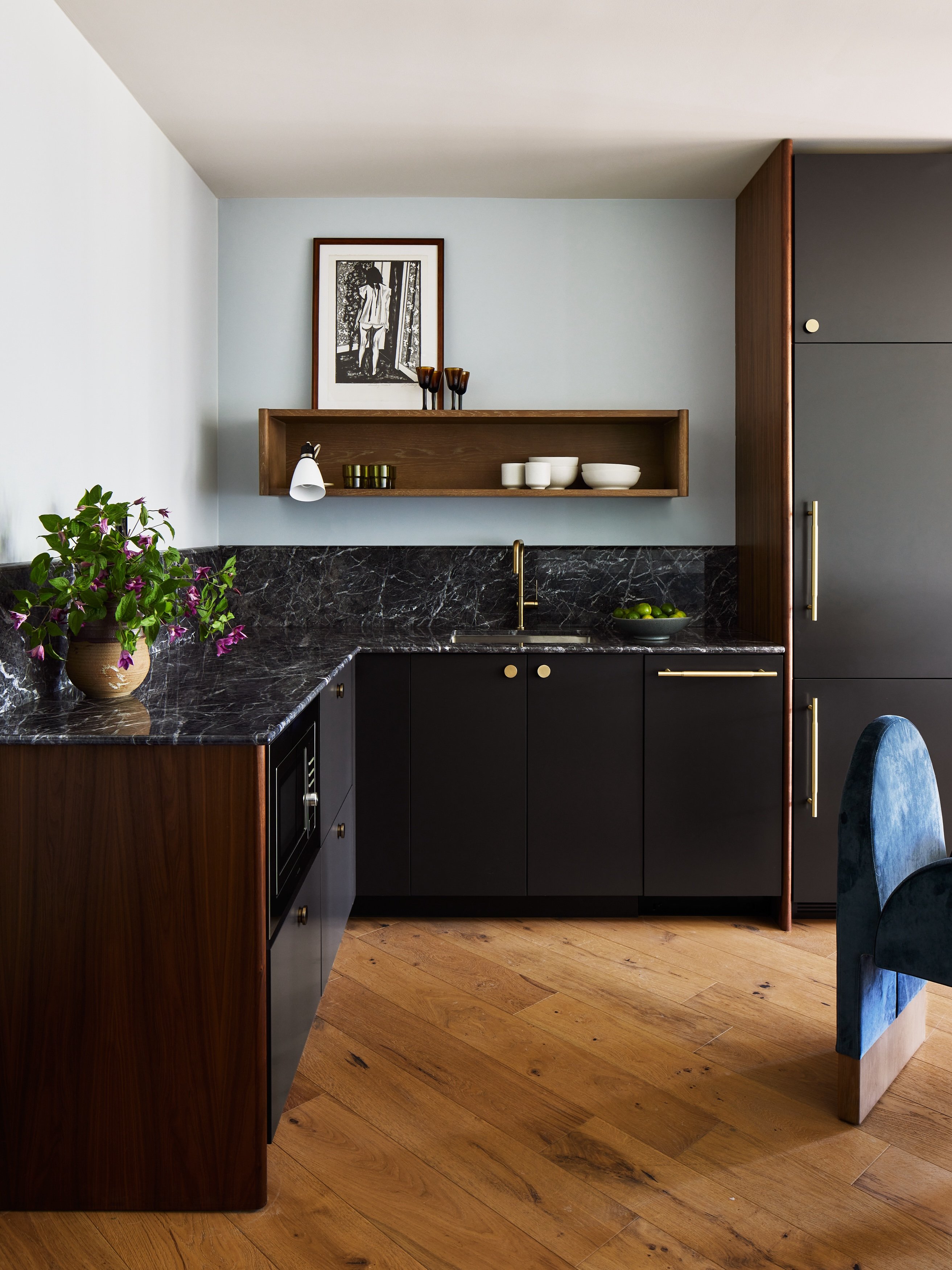 Walnut cabinetry and dramatic black marble create an intimate kitchenette where brass fixtures catch afternoon light filtering across reclaimed oak floors.
