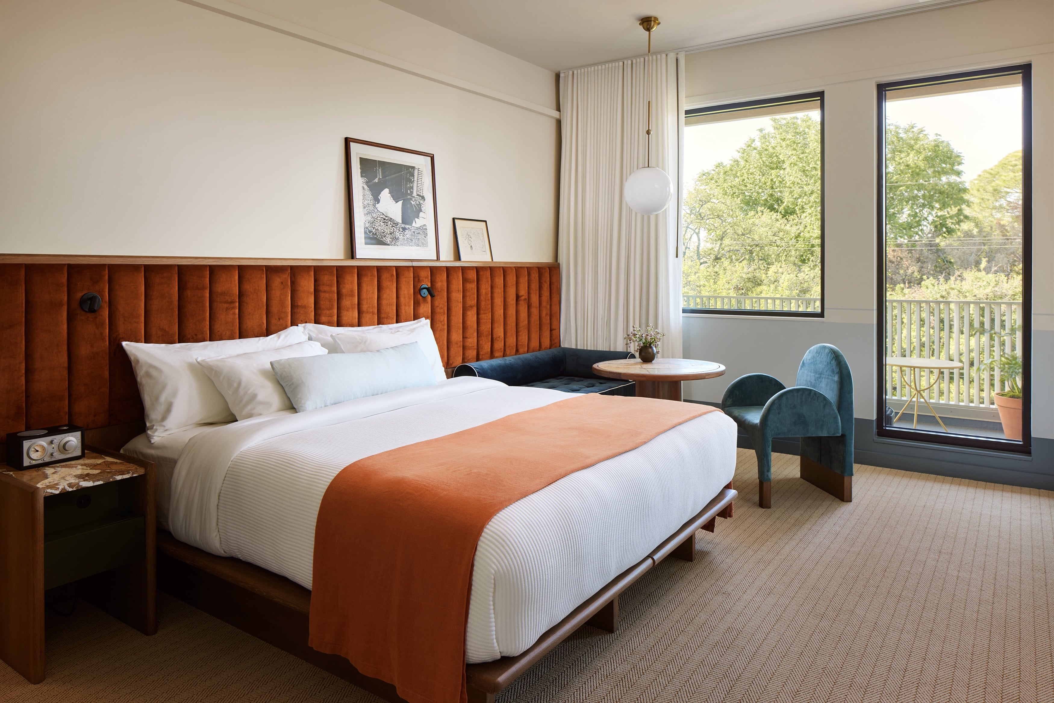 Warm wood paneling and burnt orange accents create an inviting retreat, while floor-to-ceiling windows frame leafy treetop views from the private balcony beyond.