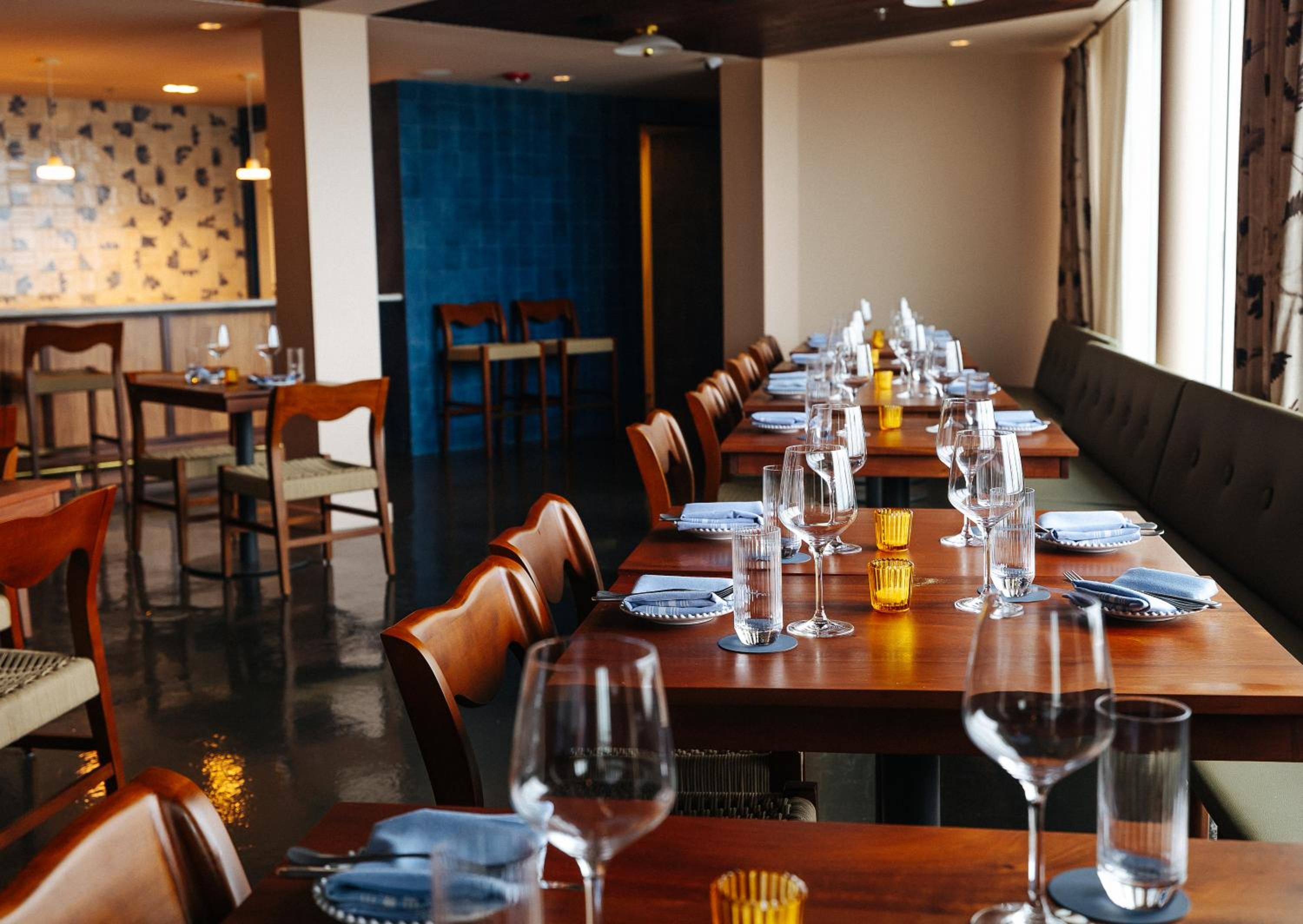 Warm leather chairs and rich walnut tables create an intimate dining atmosphere, where golden votive candles flicker against the sophisticated teal accent wall.