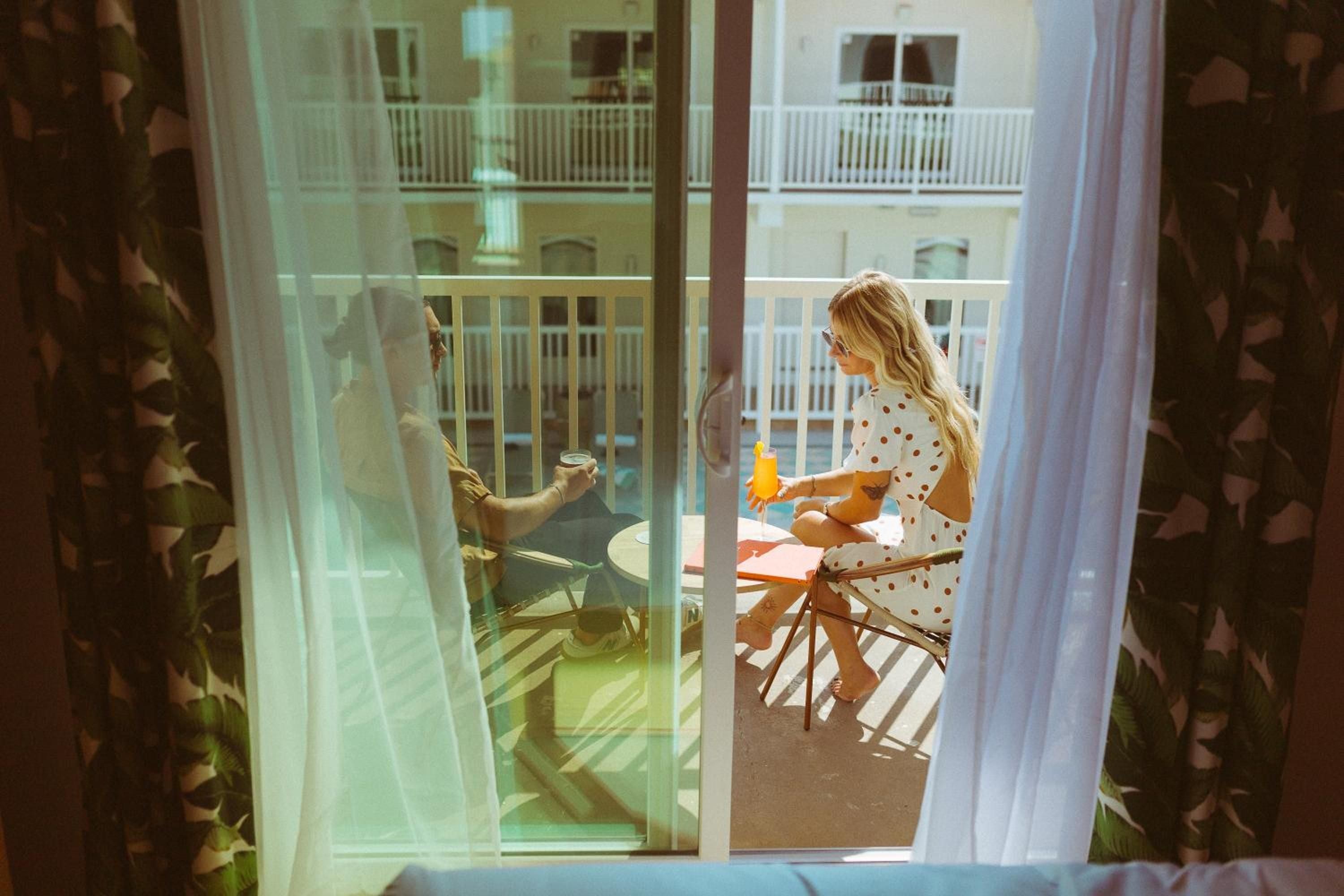 Sunlight streams through sheer curtains as a guest savors morning coffee on her private balcony, overlooking the charming courtyard architecture beyond.