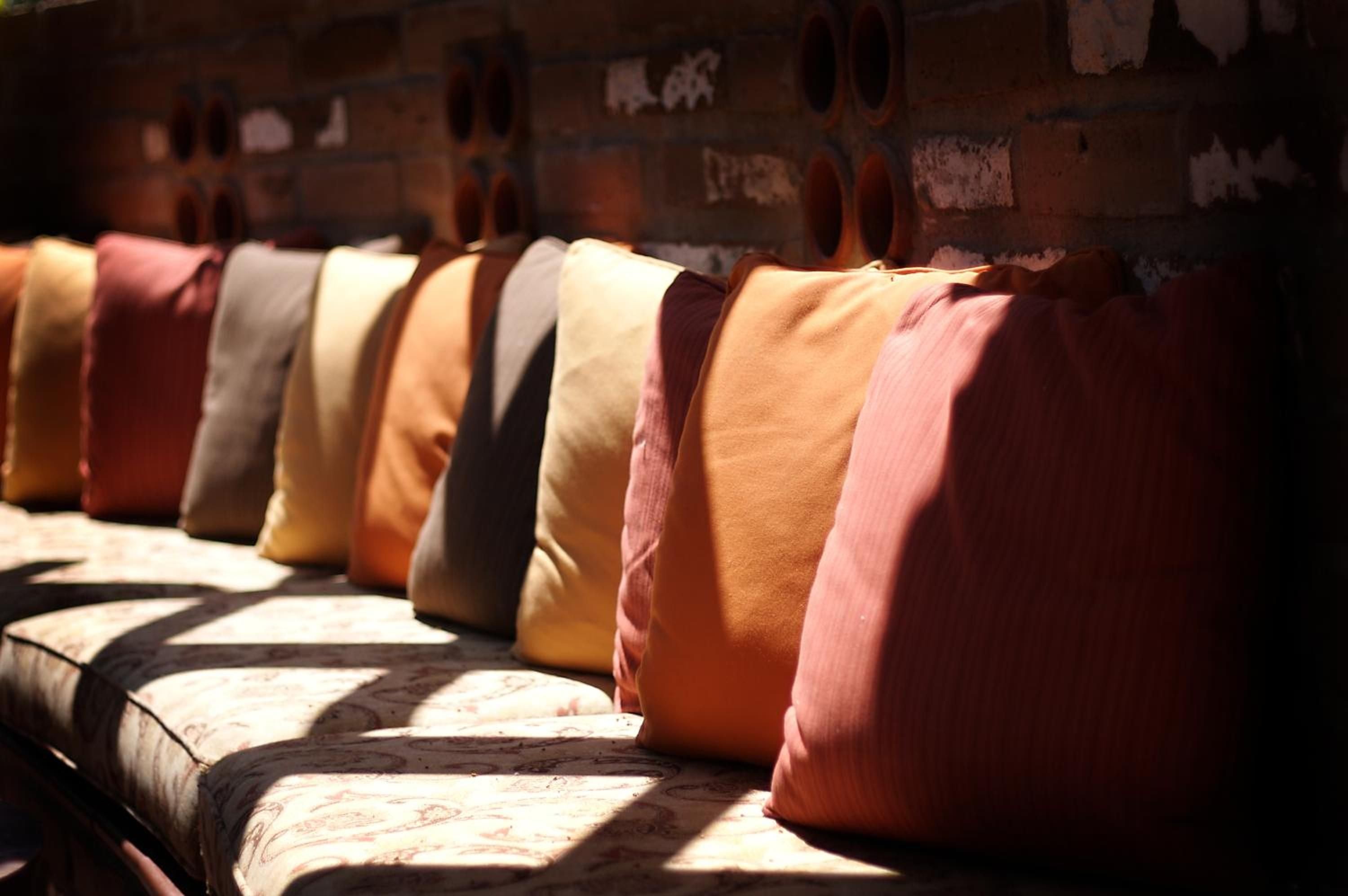 Sunlight streams across hand-woven cushions in warm terracotta and sage, creating an inviting mosaic of textures on the resort's signature banquette seating.