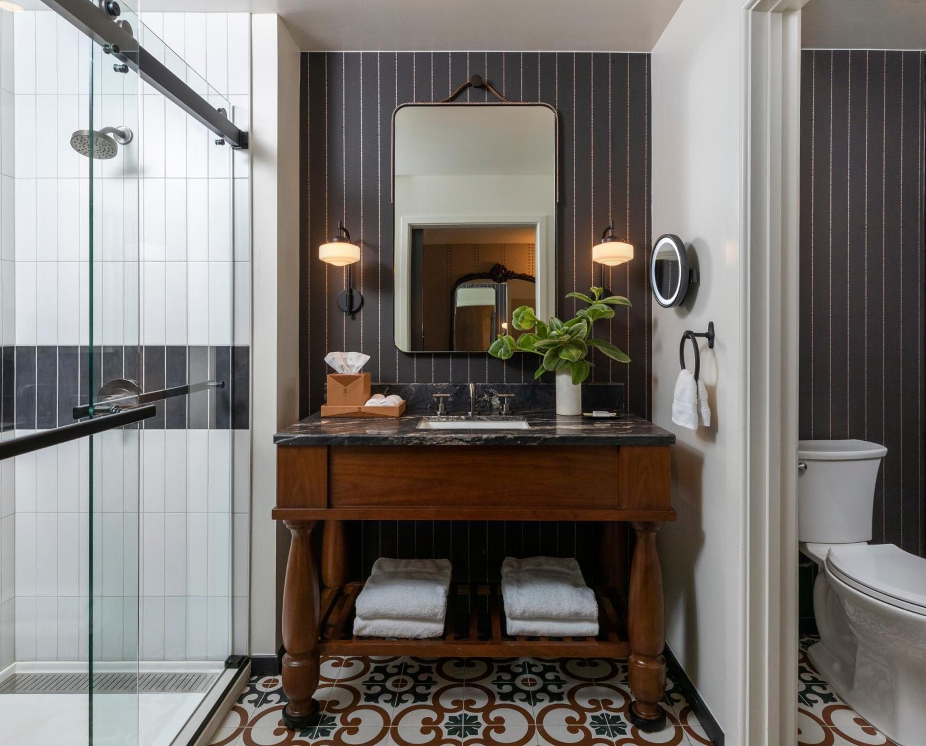 Warm wood vanity meets geometric tile floors in this sophisticated bathroom, where pendant lights cast an intimate glow over marble countertops and carefully curated details.