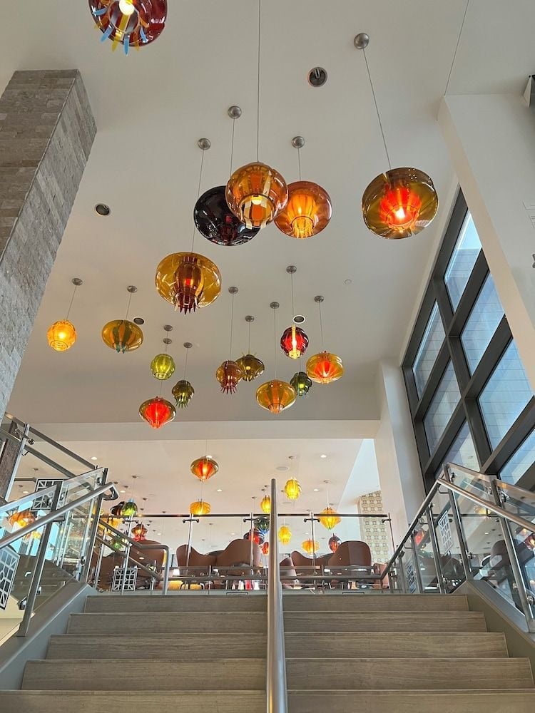 Colorful blown glass pendant lights cascade like suspended jewels above the hotel's modern staircase, creating an artful interplay of amber, crimson, and golden hues against crisp white walls.