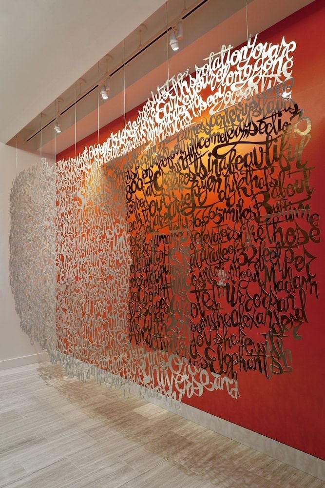 Cascading script in warm reds and oranges transforms a corridor wall into poetry in motion, where handwritten words seem to spill like autumn leaves across the gallery space.