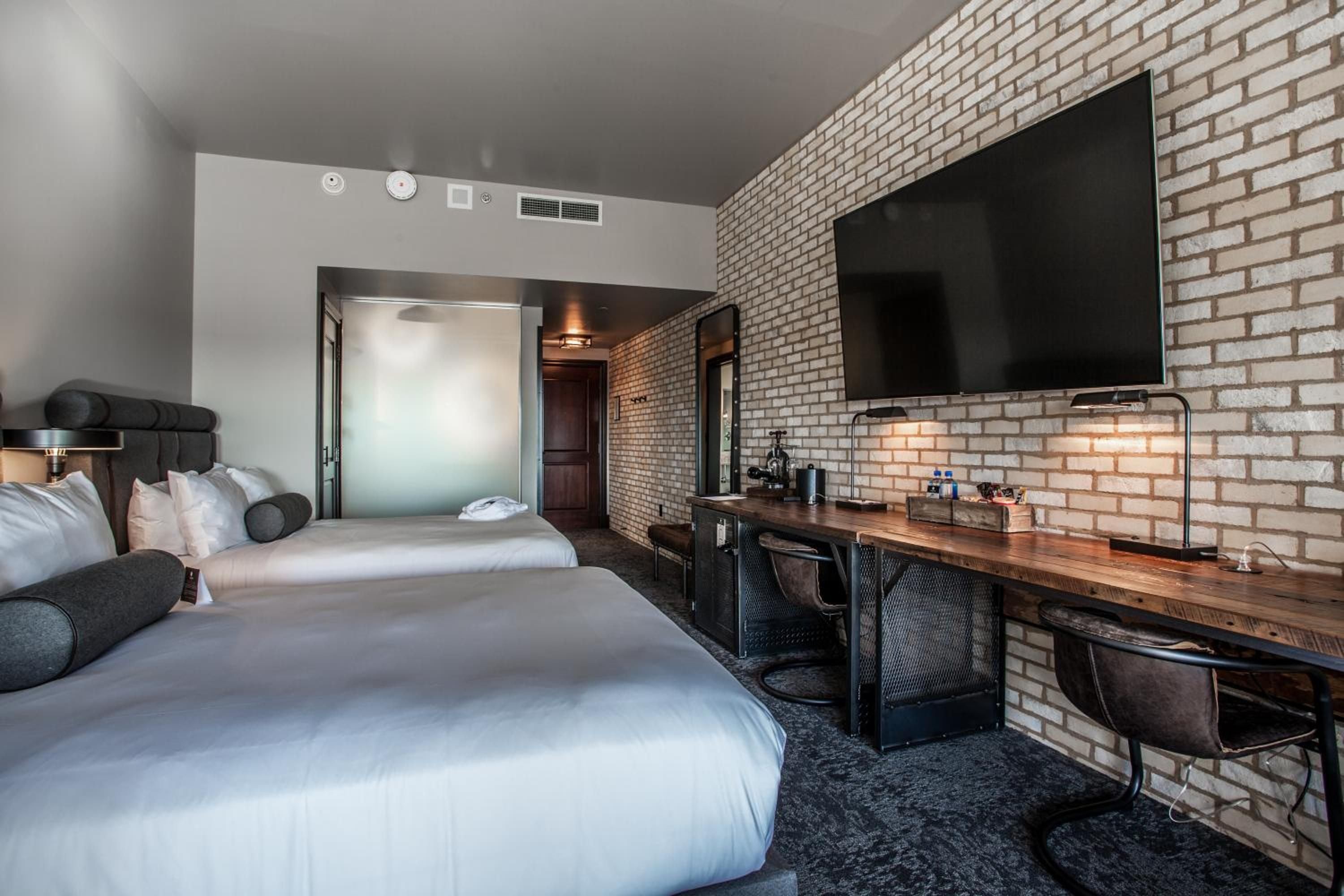 Exposed brick walls and industrial-chic furnishings create an urban sanctuary, where warm lighting illuminates handcrafted wood desks and plush bedding in this thoughtfully designed guest room.
