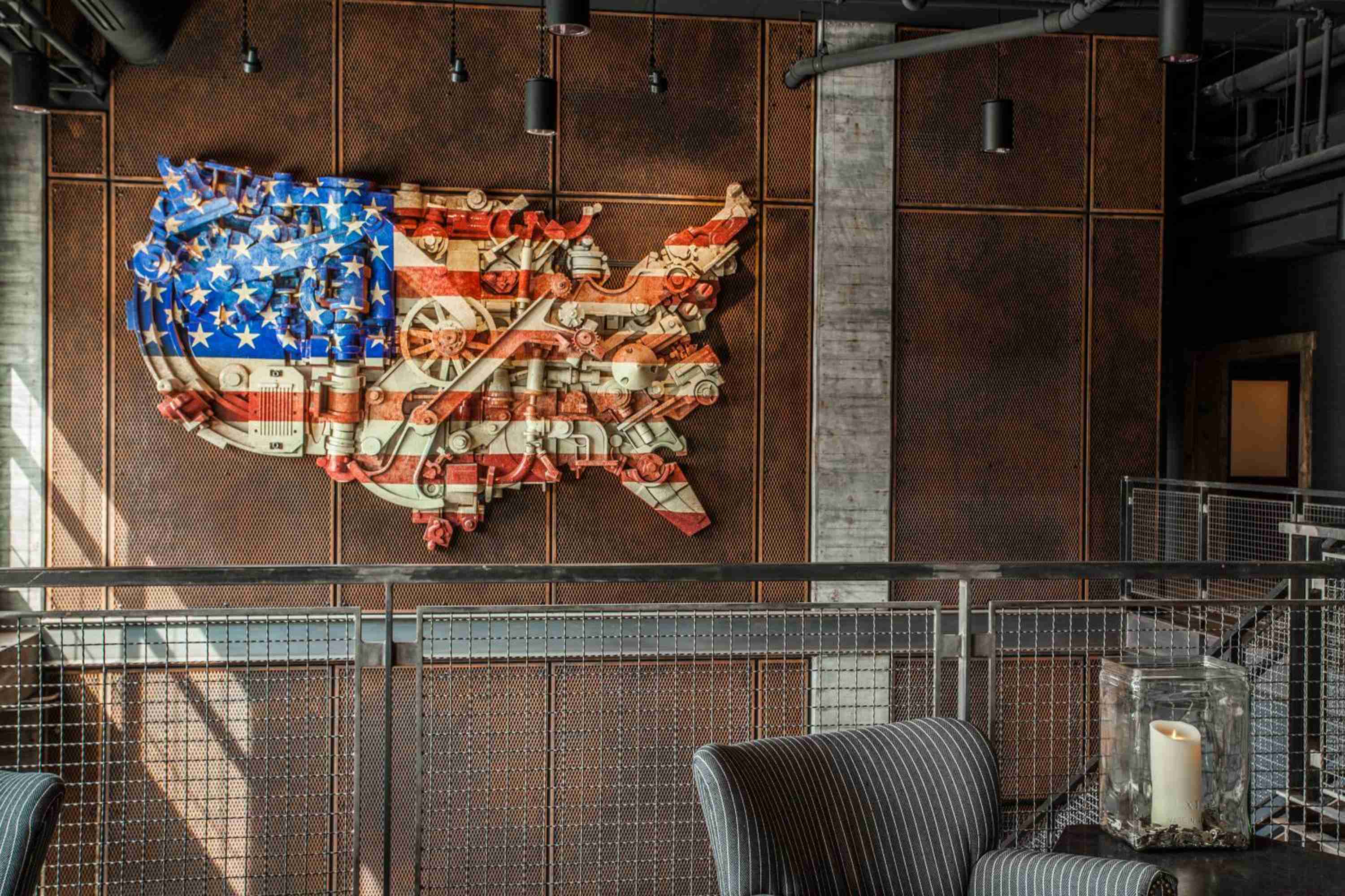 Industrial chic meets patriotic artistry in this striking bar space, where exposed metal mesh frames a bold USA map installation crafted from vintage mechanical elements.