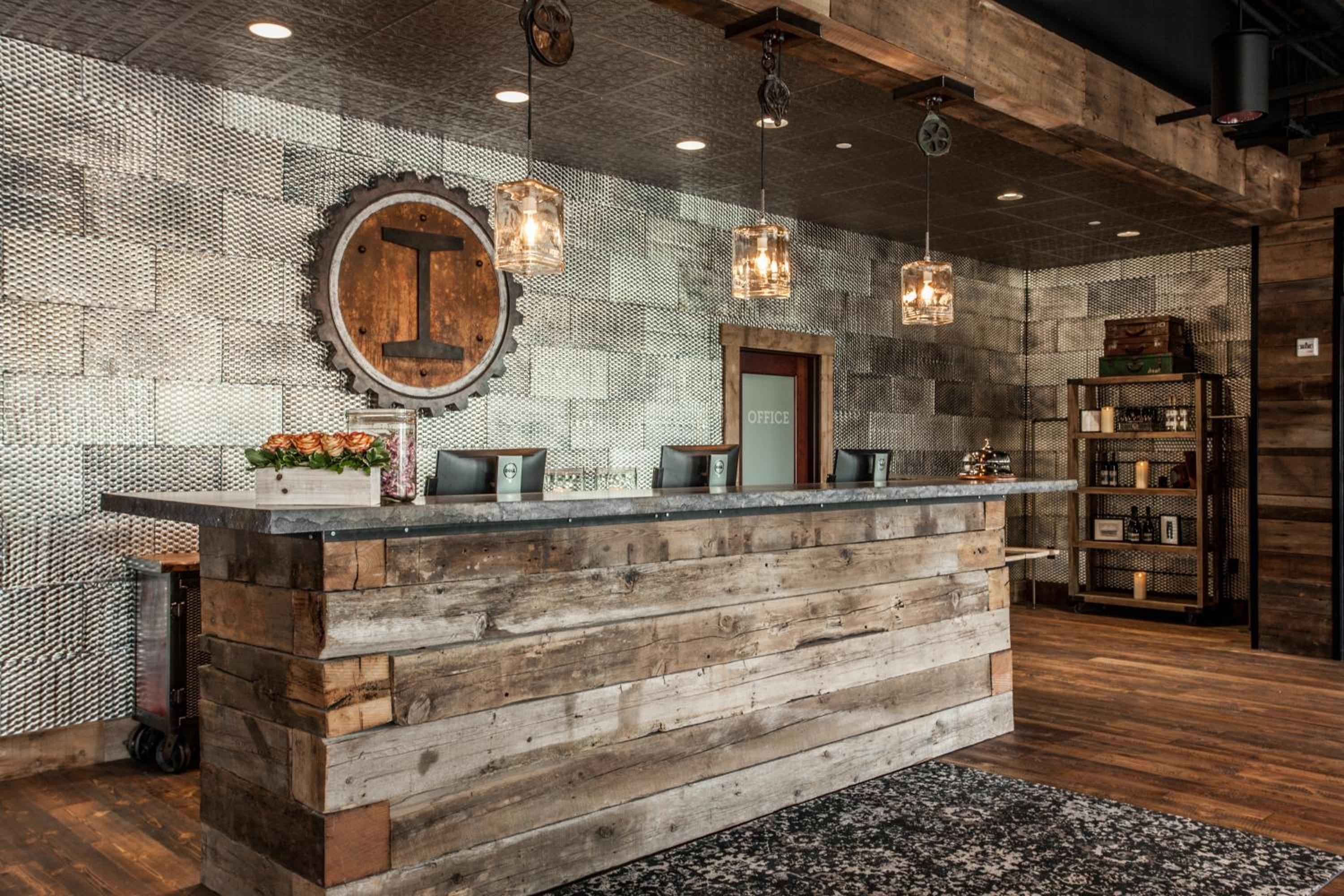 Reclaimed wood and industrial mesh create rustic sophistication at this welcoming front desk, where vintage gear-inspired signage and warm pendant lighting set an inviting tone.
