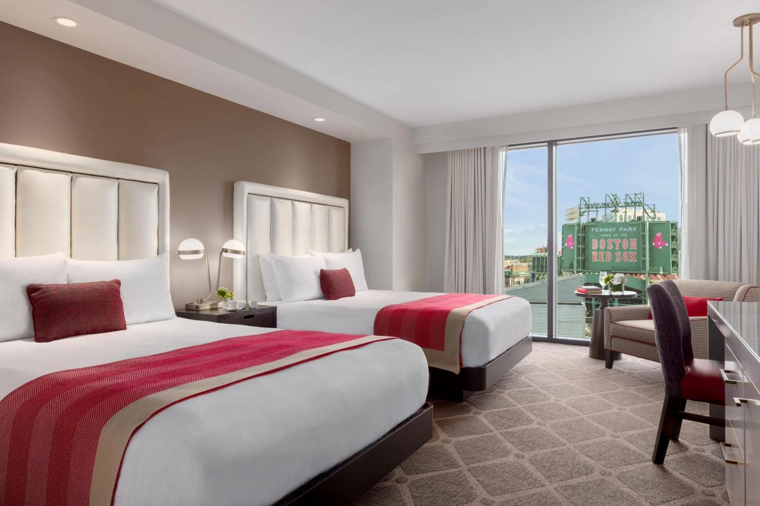 Twin beds draped in crimson accents frame floor-to-ceiling windows overlooking Fenway Park's iconic Green Monster, where baseball dreams meet boutique luxury in Boston's Kenmore Square.