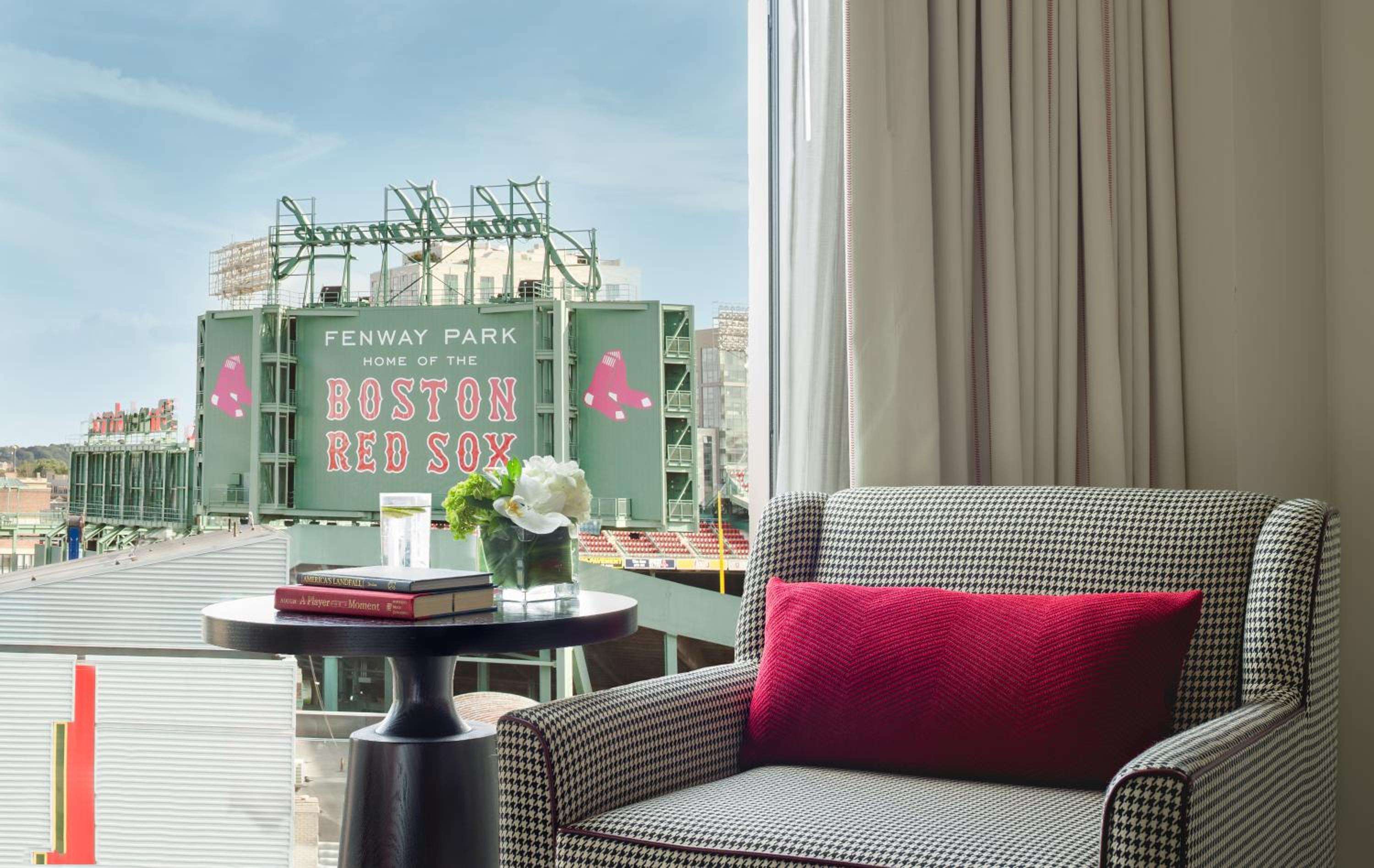 Fenway Park's iconic green facade fills the window frame while houndstooth upholstery and a crimson pillow echo Boston's baseball heritage in this perfectly positioned guest room.