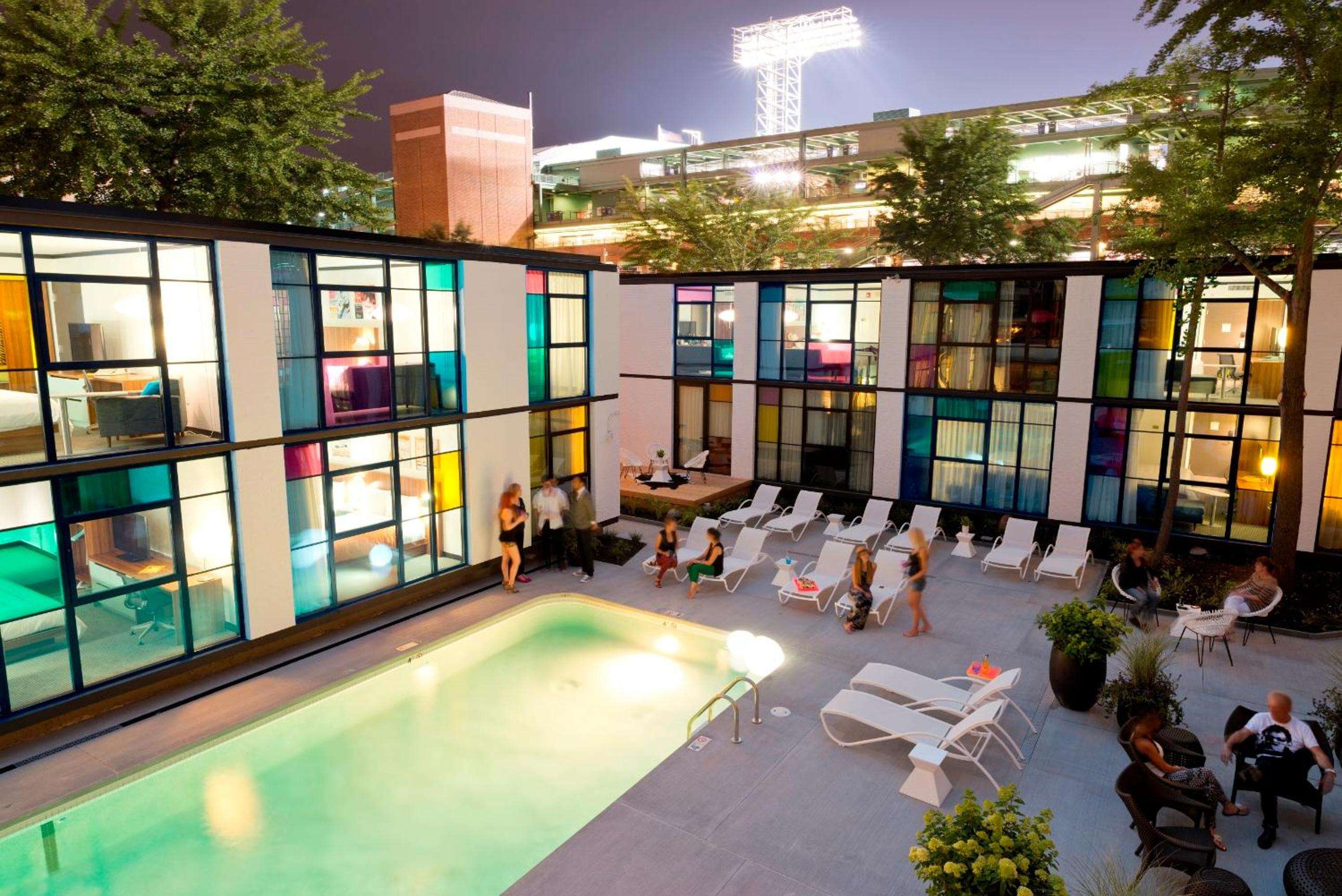 Stained glass windows in jewel tones frame the illuminated courtyard pool, where guests gather beneath stadium lights as Boston's evening energy pulses beyond.
