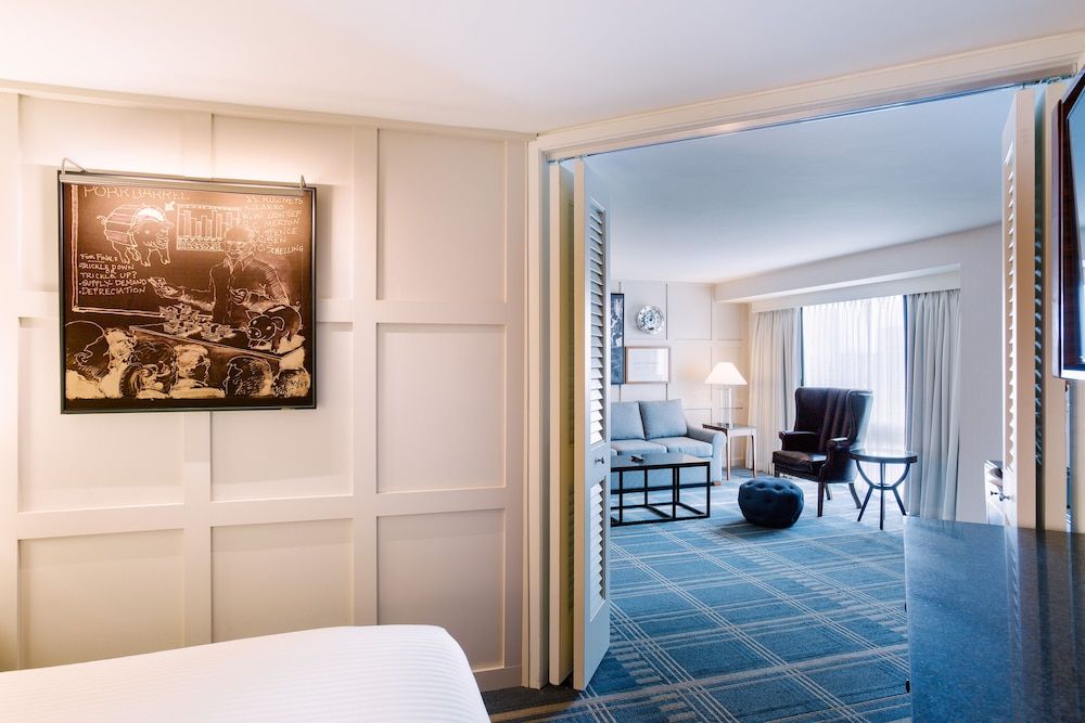 Sophisticated paneled walls and warm lighting create an intimate foyer leading to a sunlit sitting area adorned with plaid carpeting and contemporary furnishings.