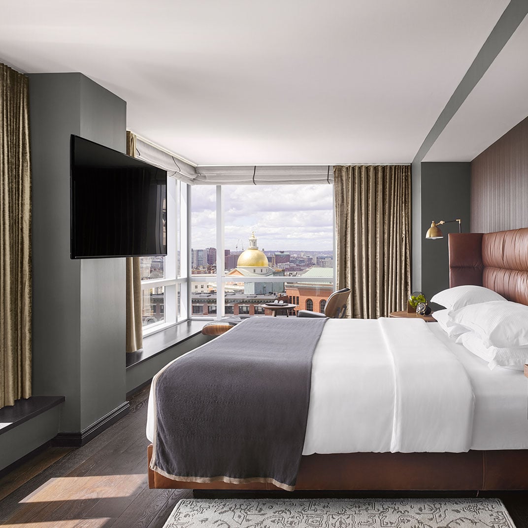 Corner suites frame Boston's golden State House dome through floor-to-ceiling windows, while rich leather headboards and charcoal accents create sophisticated urban sanctuary.