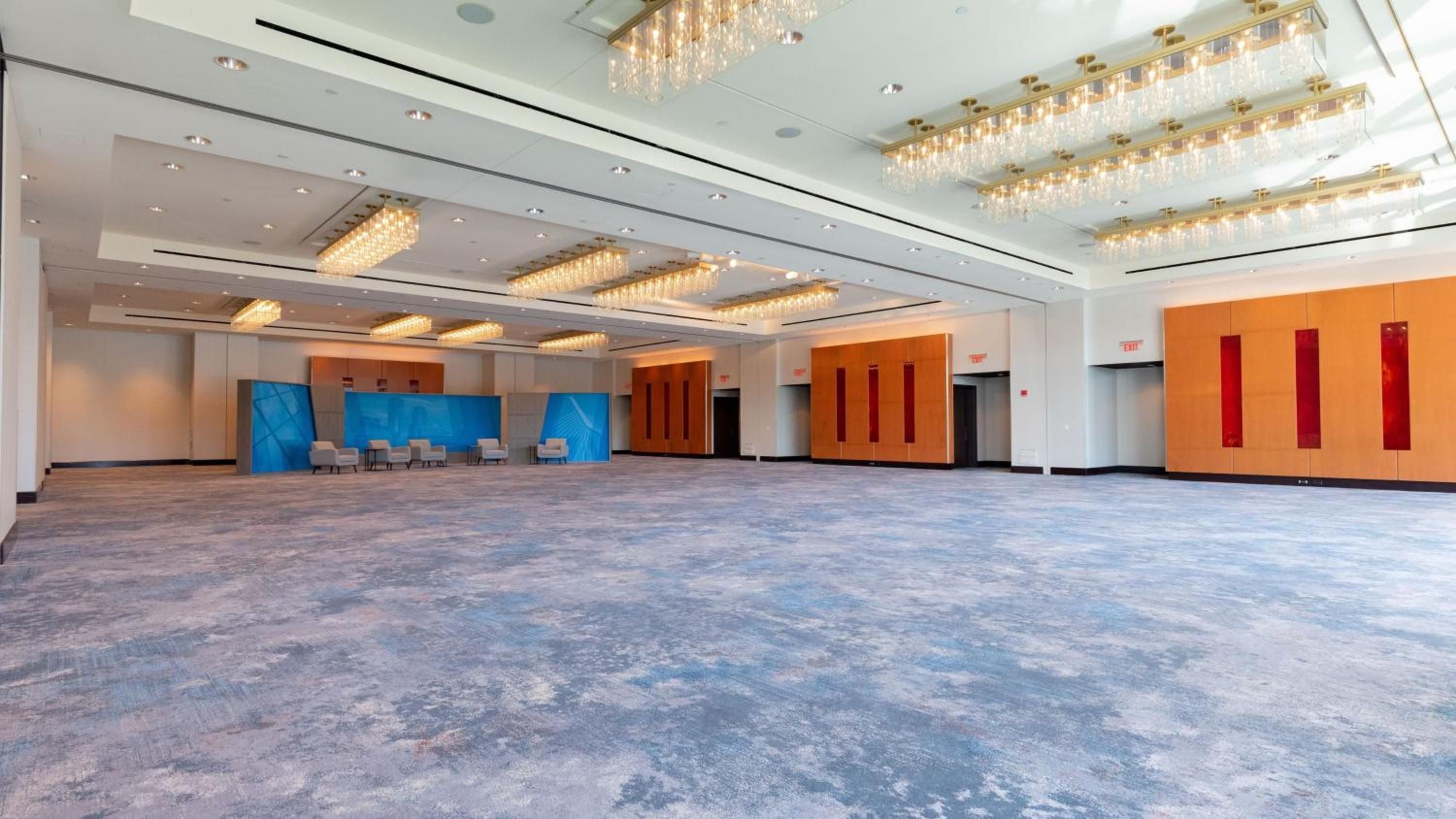Crystal chandeliers cast warm light across polished floors while vibrant blue and orange accent walls transform this expansive ballroom into an unexpectedly dynamic corporate canvas.