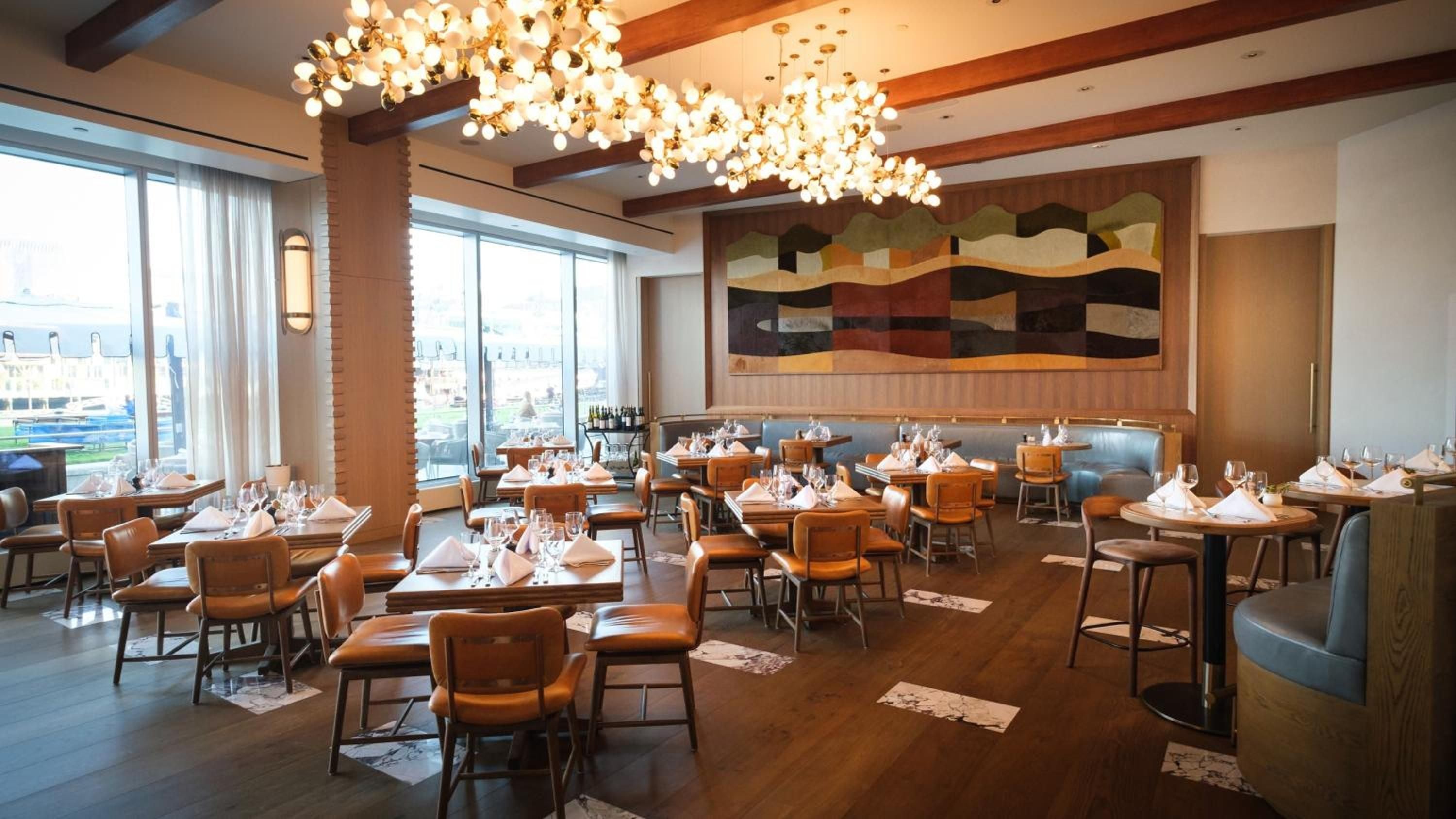 Warm leather chairs and dramatic bubble chandeliers create an inviting atmosphere in this contemporary dining room, where abstract artwork complements exposed wooden beams overhead.