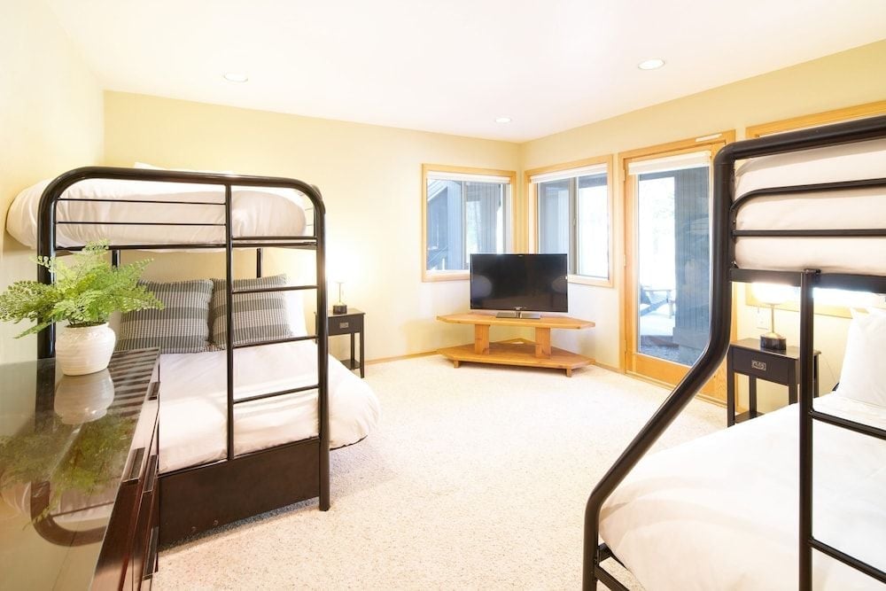 Black metal bunk beds maximize space in this bright corner room, where natural light streams through wood-framed windows onto crisp white linens and warm hardwood floors.