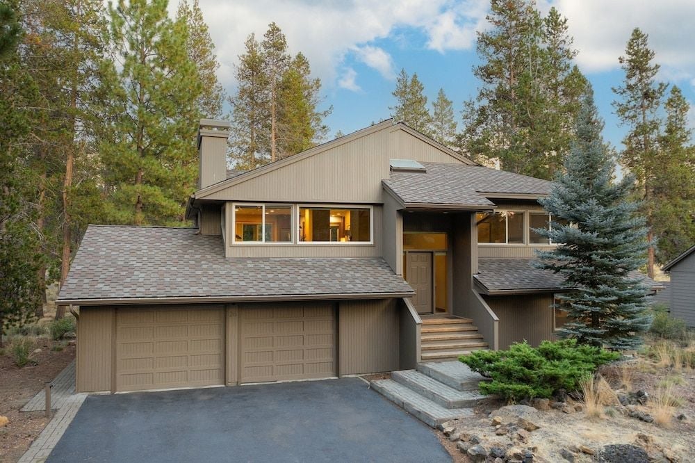 Warm light spills from oversized windows as this contemporary mountain retreat emerges from towering pines, its cedar-shingled facade and welcoming staircase promising elevated alpine luxury.