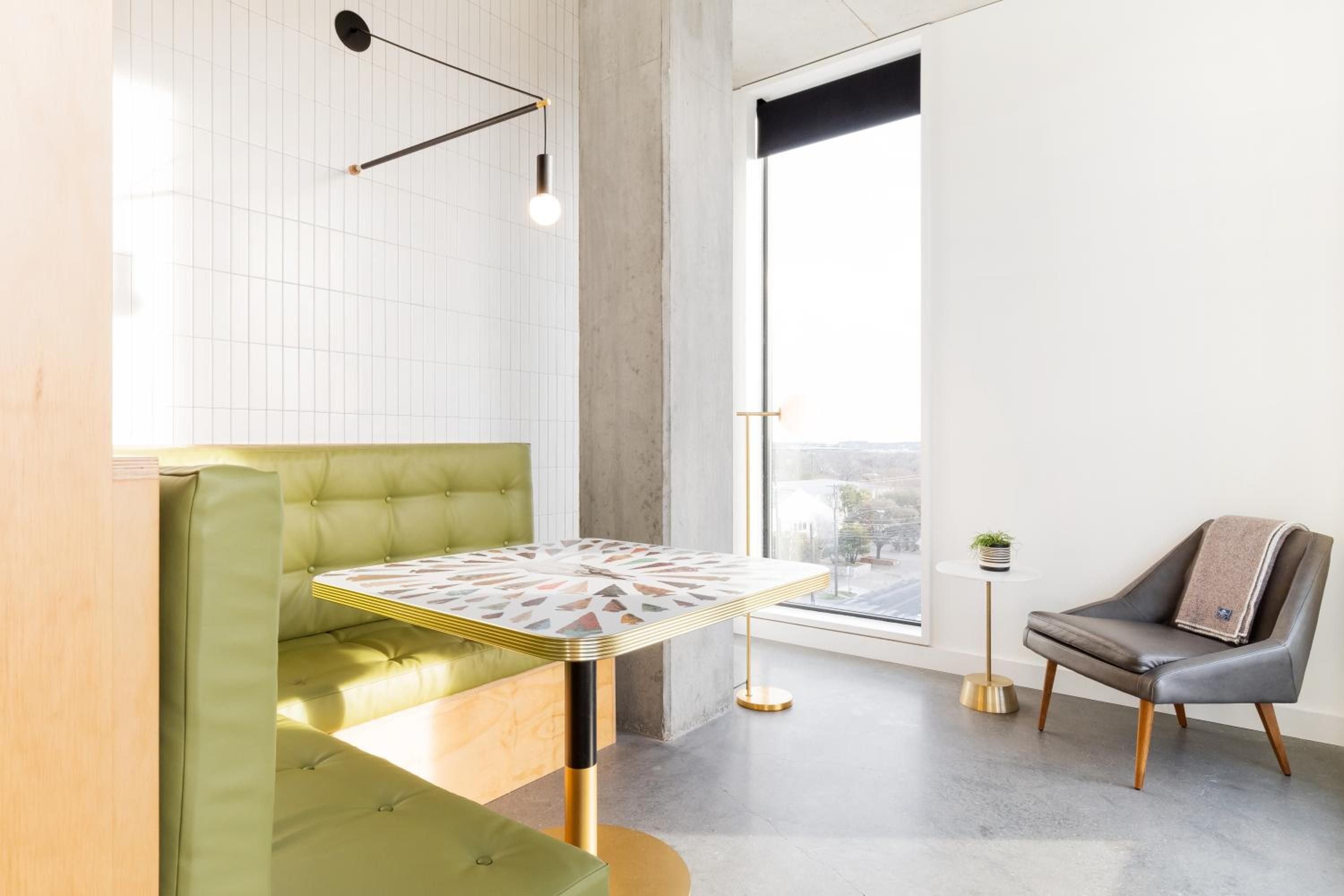 Retro-chic banquette seating in chartreuse leather anchors a corner dining nook, where terrazzo flooring meets white subway tiles beneath sculptural pendant lighting.