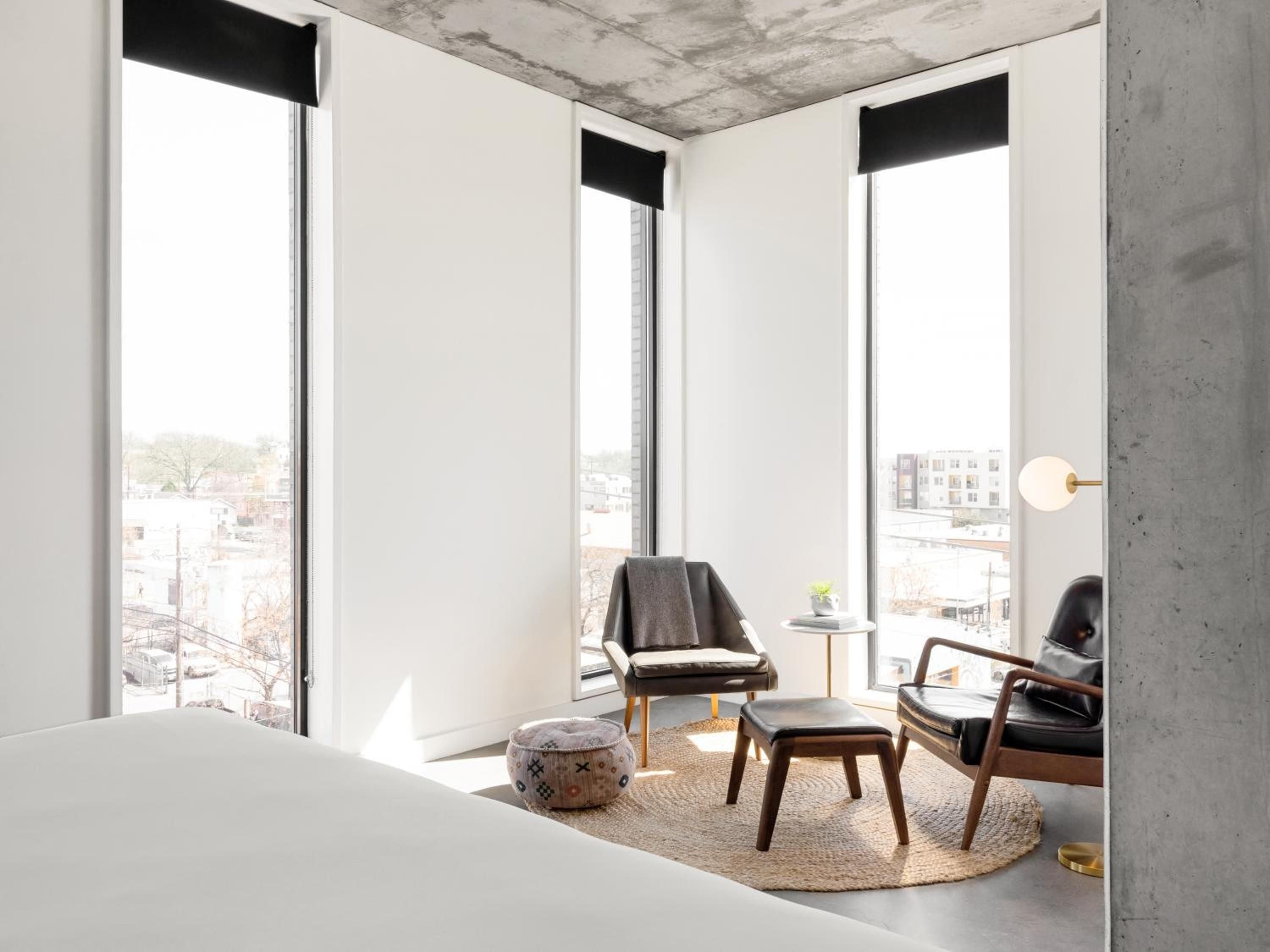 Floor-to-ceiling windows frame Austin's evolving skyline from this minimalist corner suite, where raw concrete meets walnut midcentury chairs and natural light spills across jute rugs.