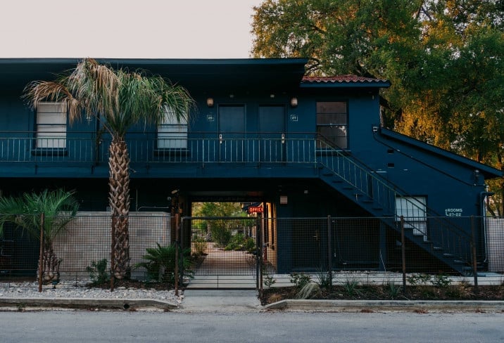 Moody blue facade and palm-lined entrance create an inviting mid-century vibe, where external staircases and thoughtful landscaping hint at the property's reimagined desert charm.