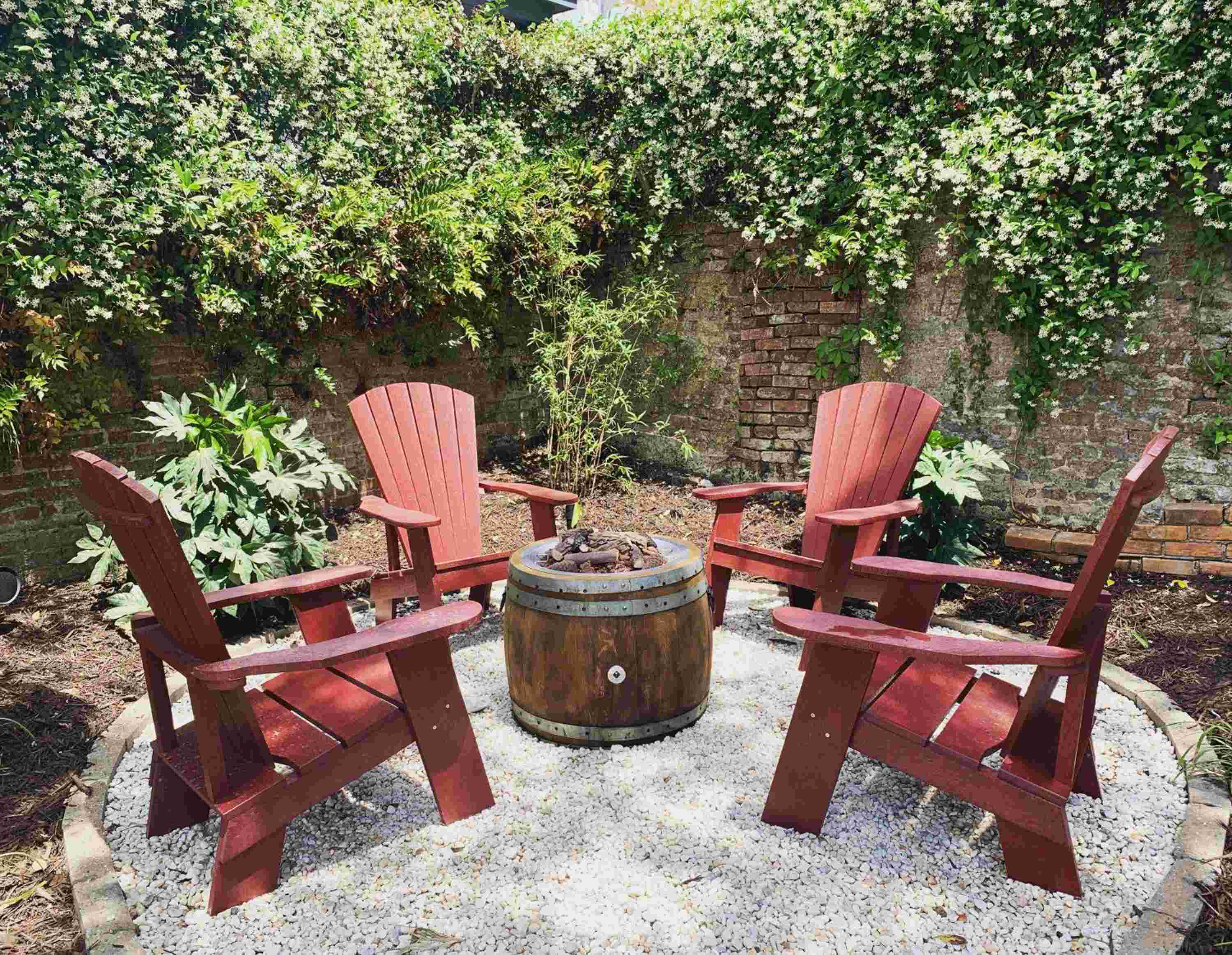 Weathered Adirondack chairs circle a rustic barrel planter in this intimate garden nook, where ivy-draped brick walls create a secret courtyard feeling.