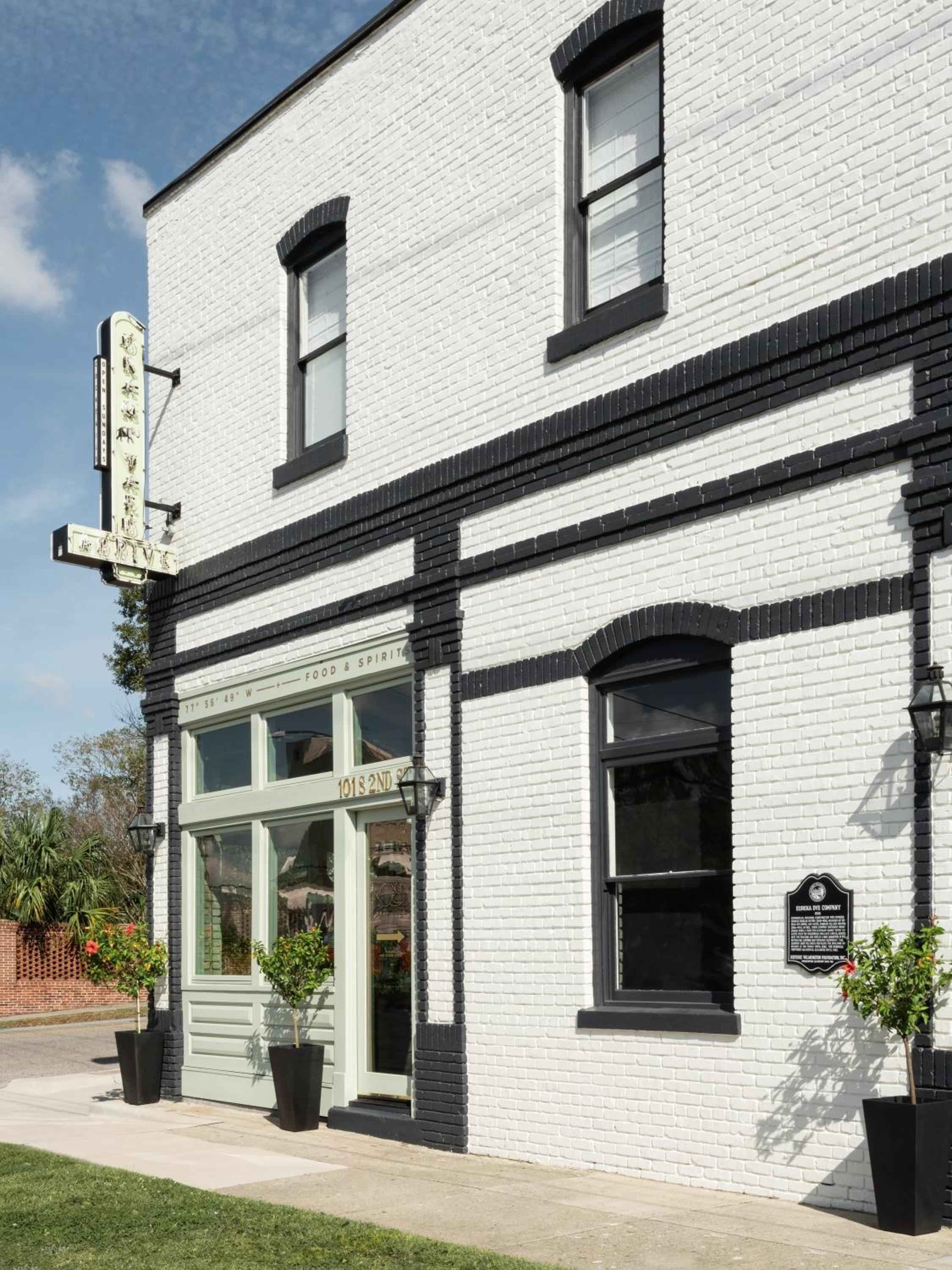 Crisp white brick and sage green trim define this charming corner bistro, where potted plants and vintage signage create an inviting neighborhood gathering spot.