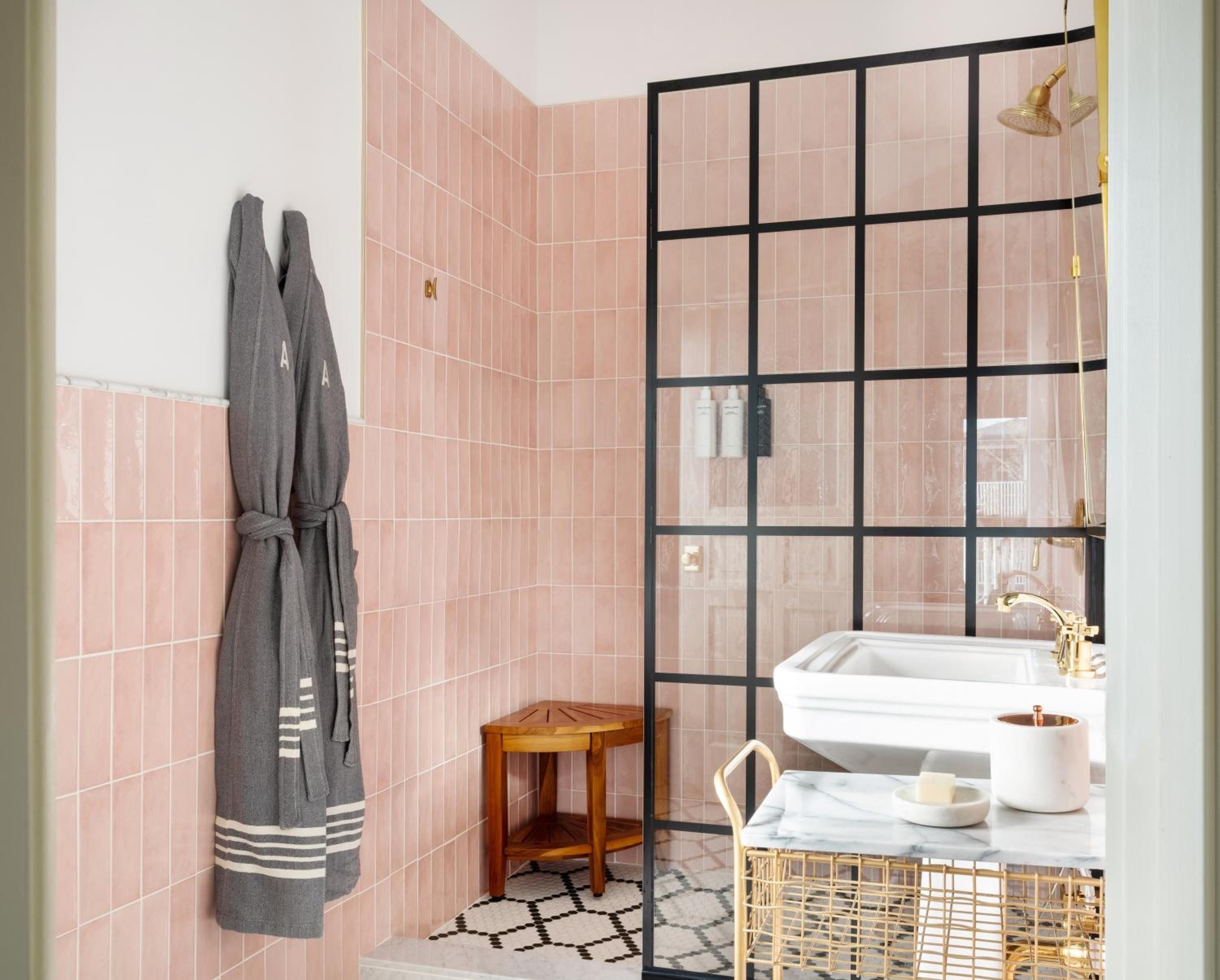 Blush pink tiles and black gridded glass create an unexpectedly chic shower moment, where brass fixtures gleam against thoughtfully curated textures and striped linens.
