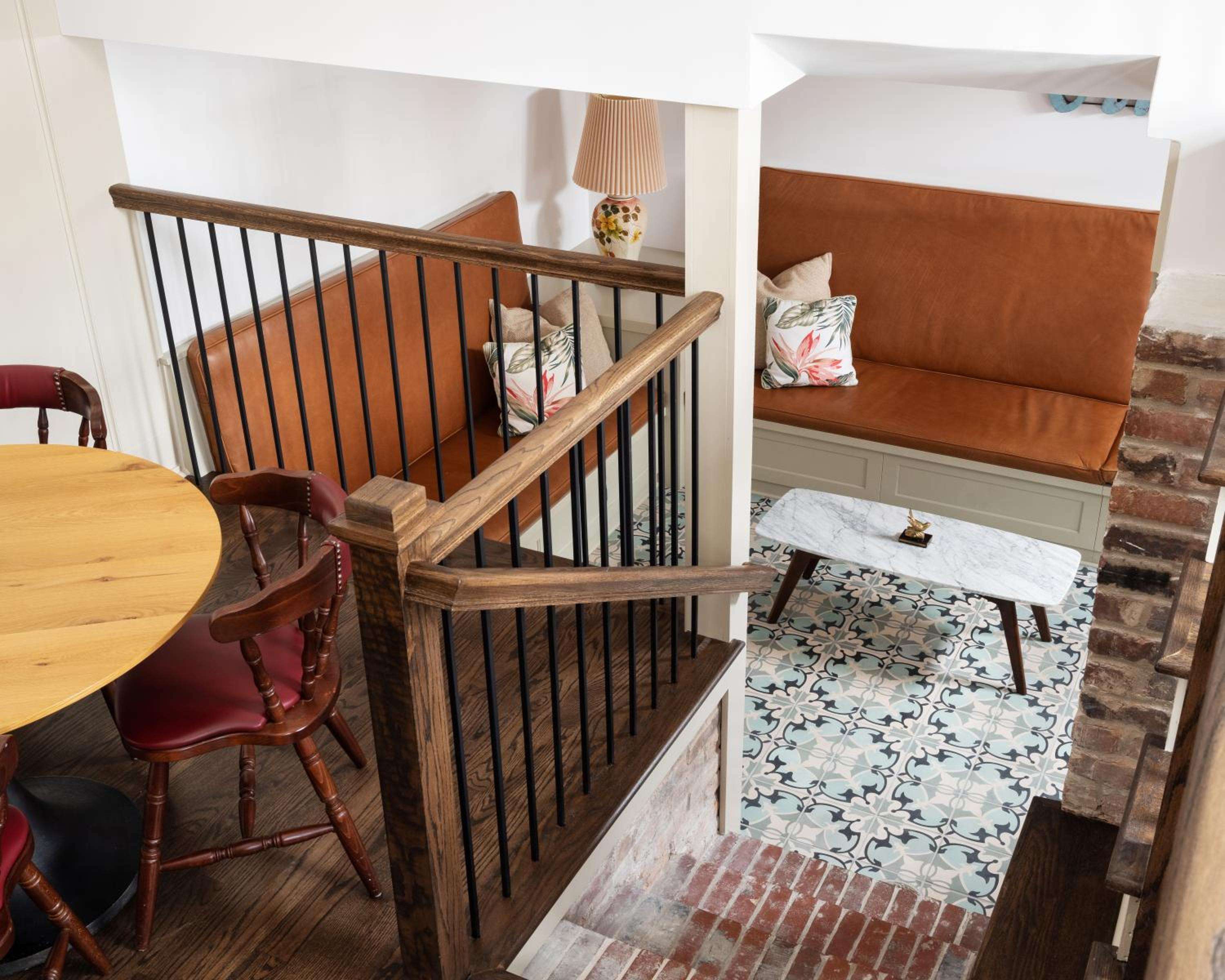 Split-level seating areas blend exposed brick charm with modern comfort, where burnt orange banquettes and patterned tiles create intimate conversation nooks beneath warm lamplight.