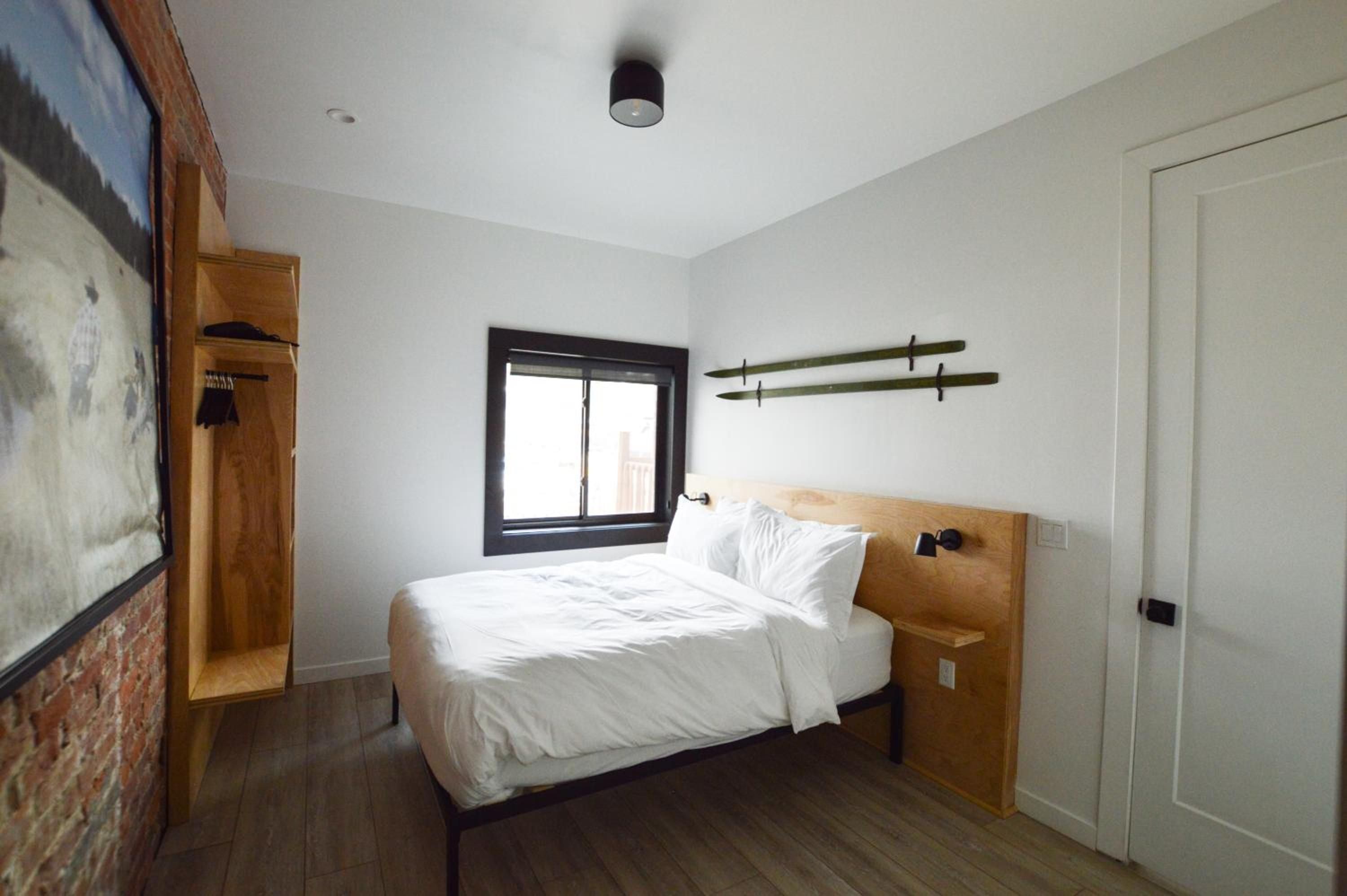 Warm wood accents and surfboard wall art create a cozy retreat where exposed brick meets modern minimalism in this thoughtfully designed guest room.