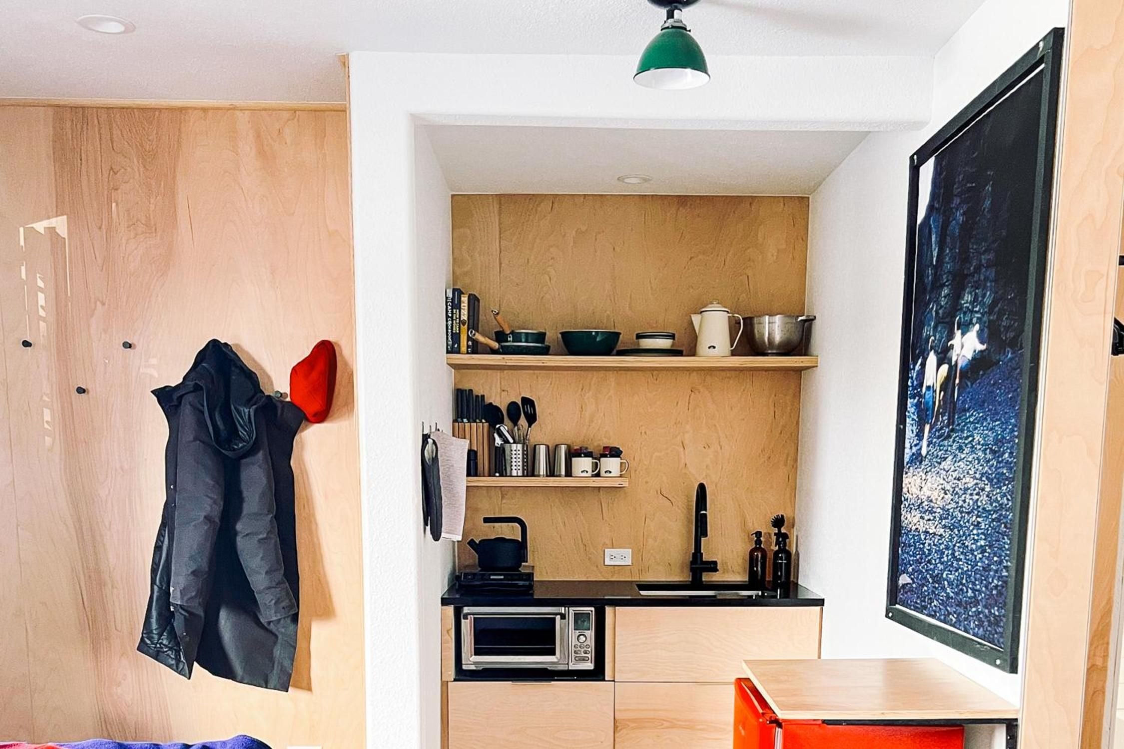 Blonde wood cabinetry and clever storage maximize every inch of this compact kitchenette, where a green pendant light casts warm shadows over thoughtfully curated dishware.
