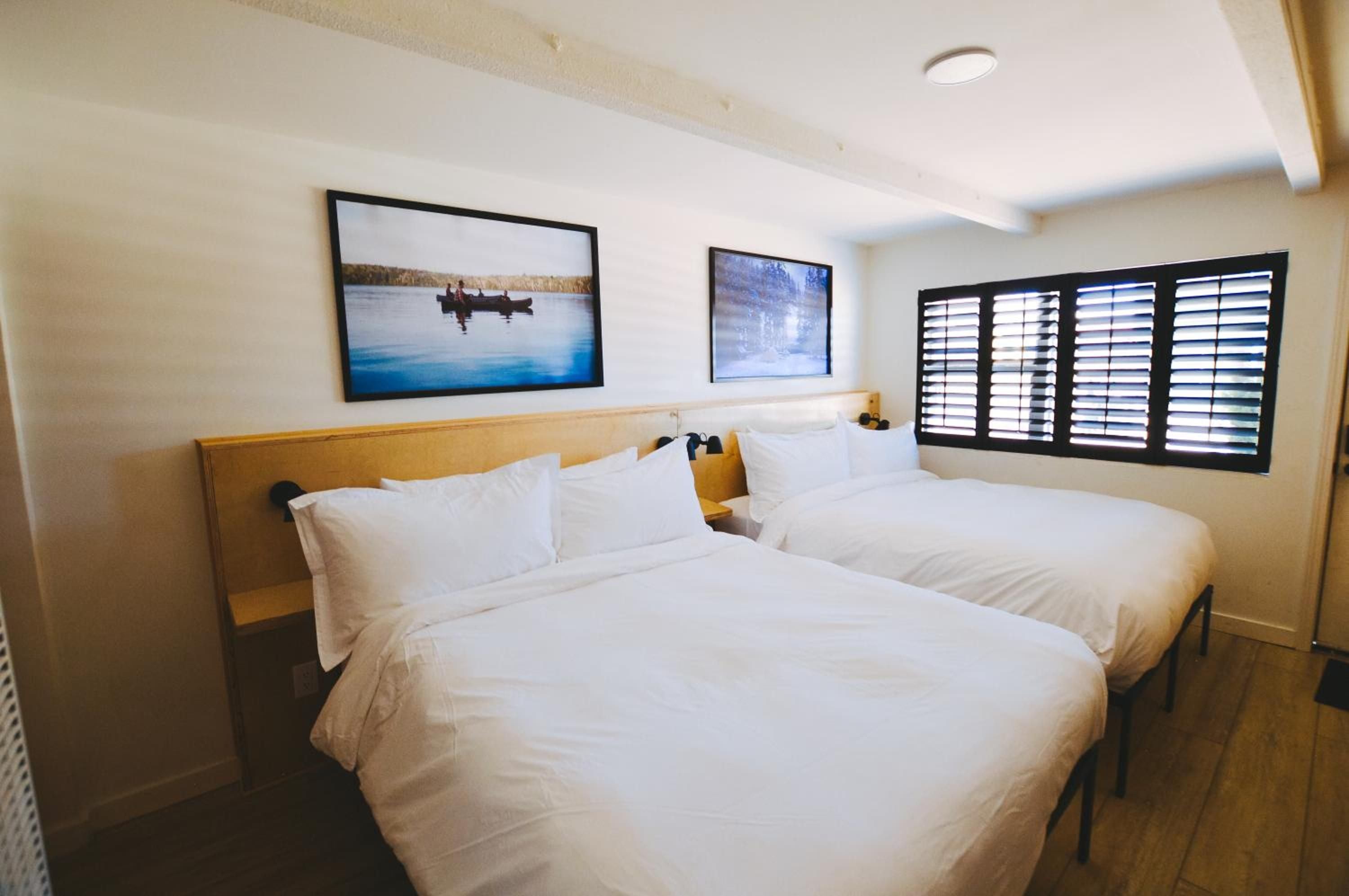 Twin beds with crisp white linens frame tranquil lake artwork, while plantation shutters filter soft natural light across warm wood finishes in this thoughtfully appointed guest room.