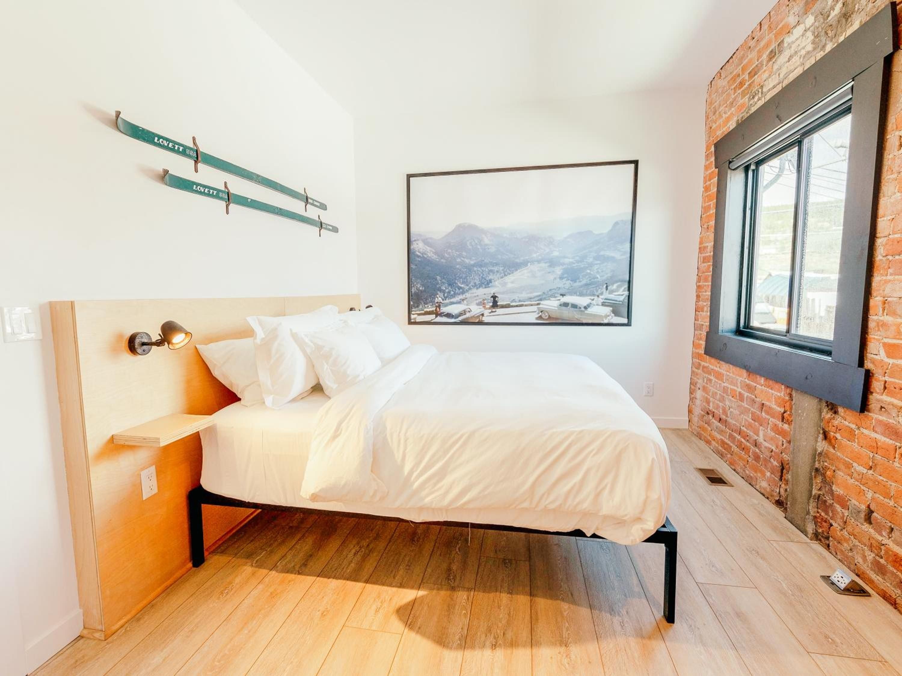 Exposed brick walls and vintage ski equipment create alpine charm in guest rooms, where crisp white linens meet warm wood floors and mountain photography sets the mood.