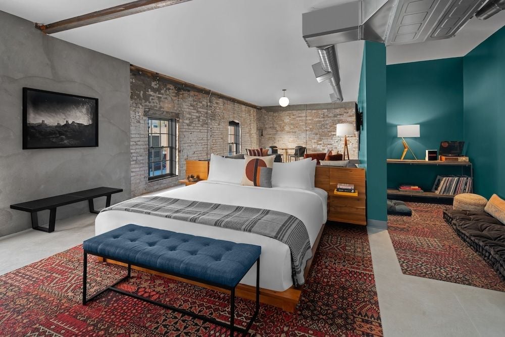 Exposed brick meets bold teal walls in this industrial-chic suite, where vintage Persian rugs soften concrete floors and natural light streams through steel-framed windows.