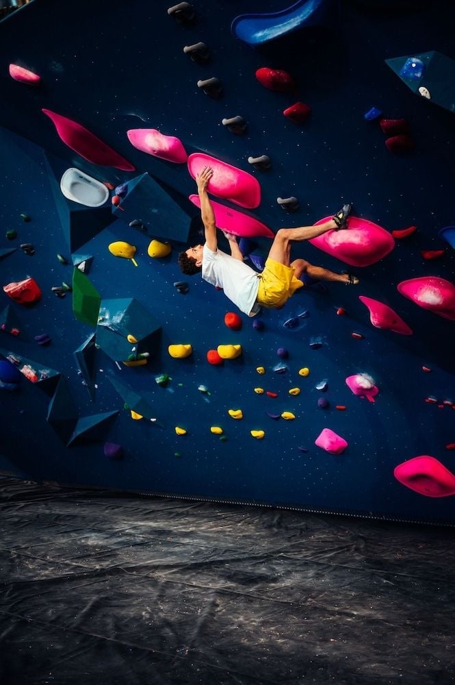 Climbers navigate vibrant holds on the overhanging bouldering wall, where neon pink and yellow grips create an artistic canvas against deep blue surfaces.