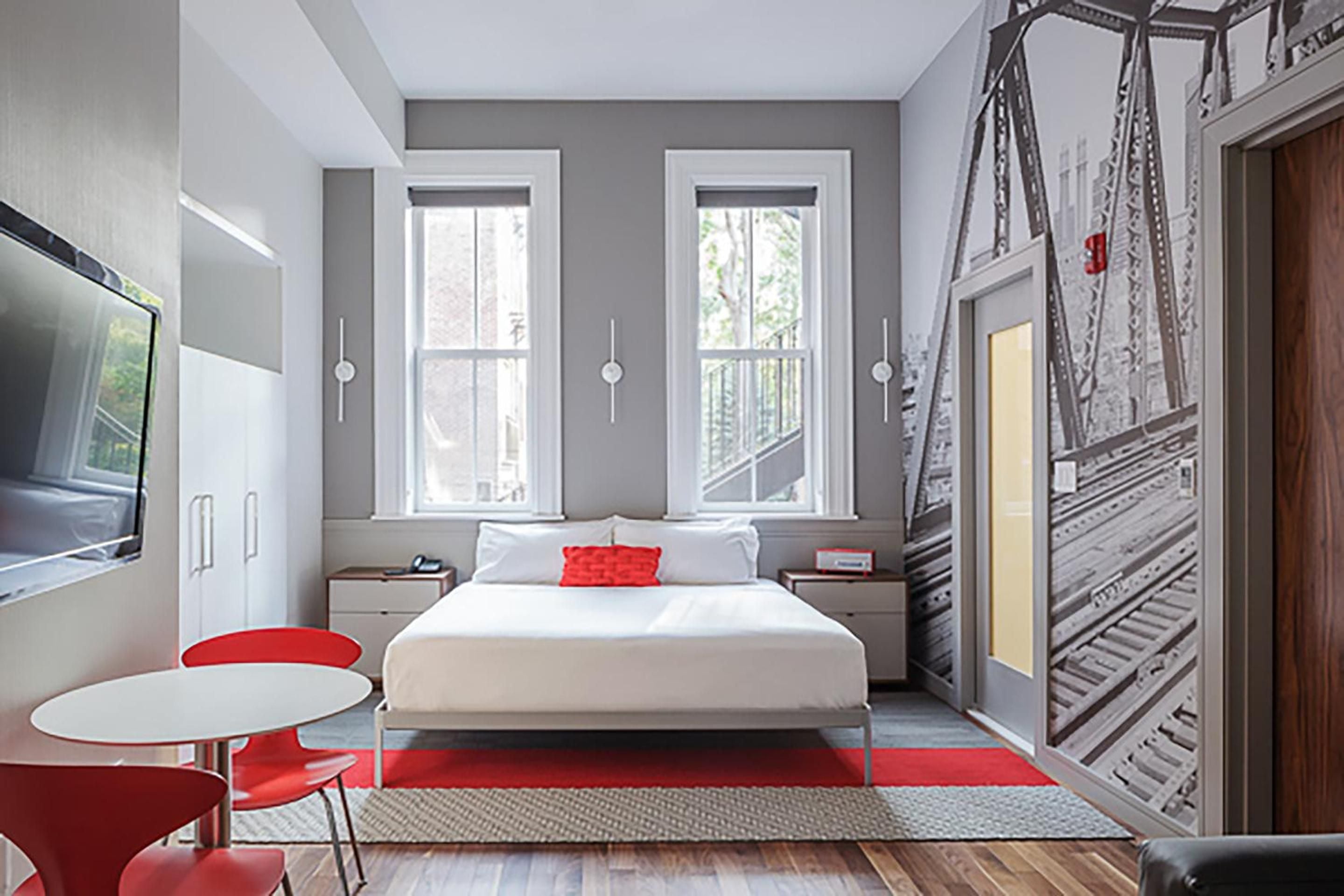 Industrial-chic meets comfort in this thoughtfully designed guest room, where exposed steel beams frame crisp white linens and pops of crimson energy.
