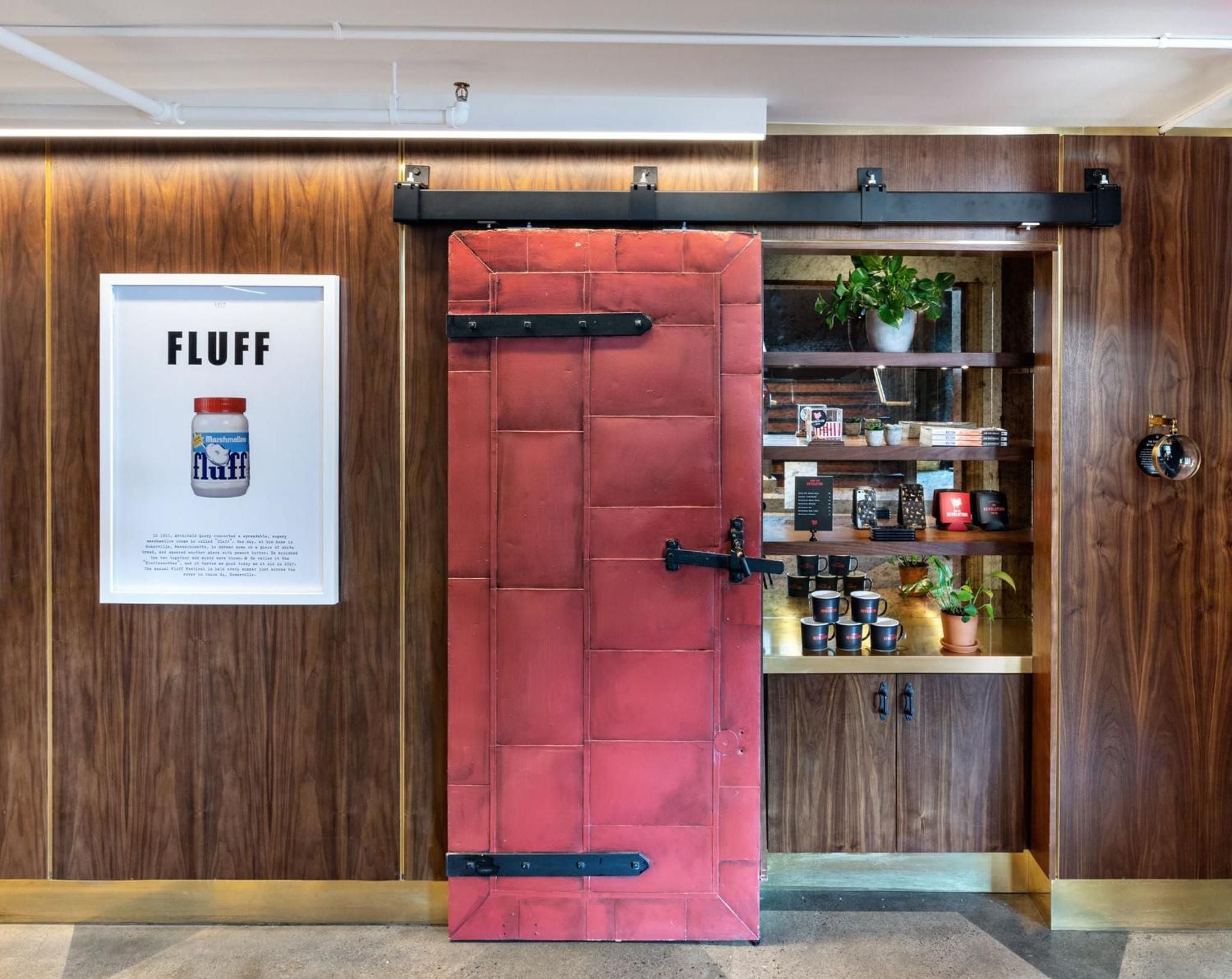 Rich walnut paneling frames a bold crimson sliding barn door, revealing curated shelving where vintage finds and modern touches create an unexpectedly sophisticated common space.