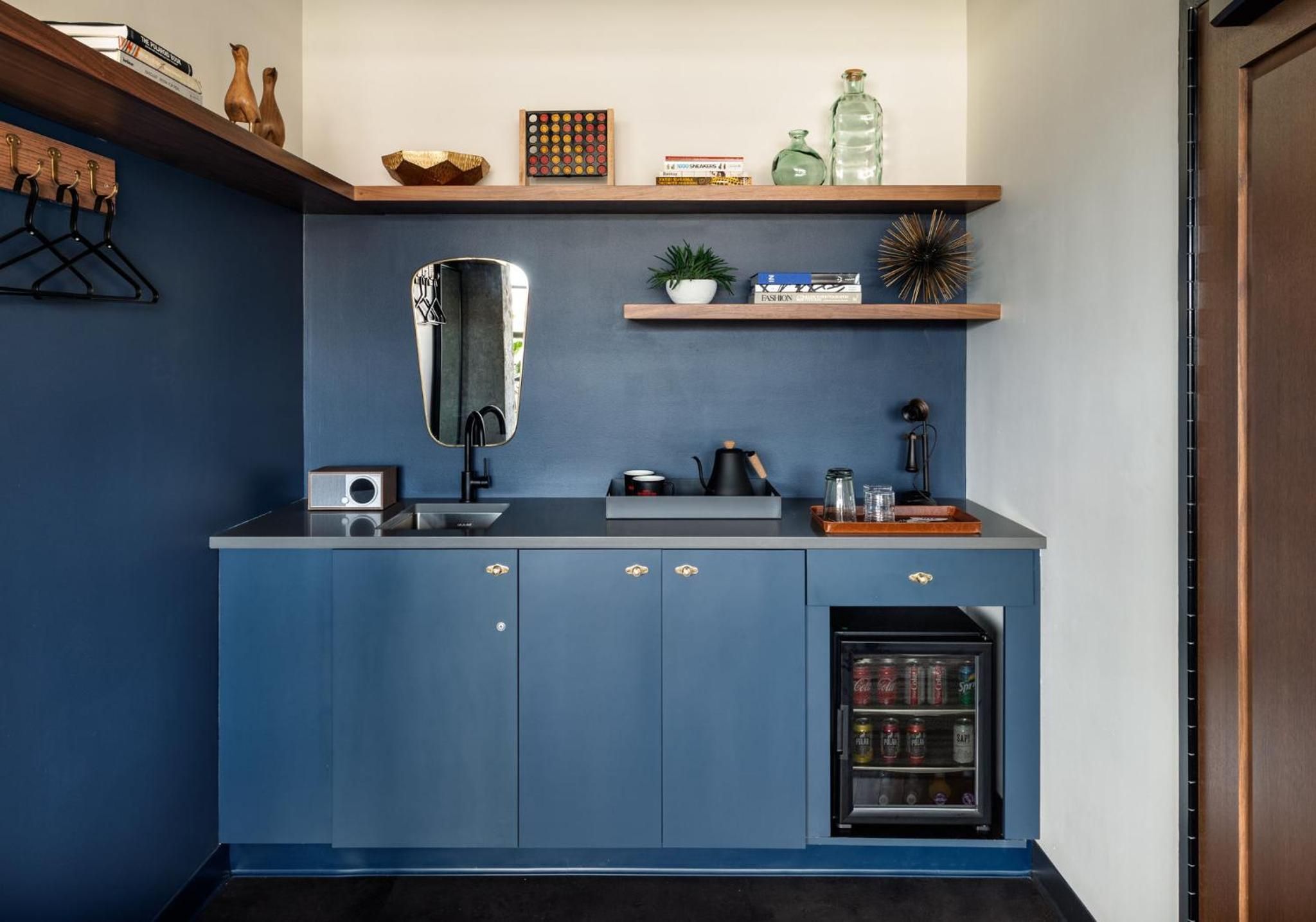 Navy blue cabinetry and warm wood shelves create a sophisticated kitchenette where brass hardware catches morning light filtering through this thoughtfully designed guest room.
