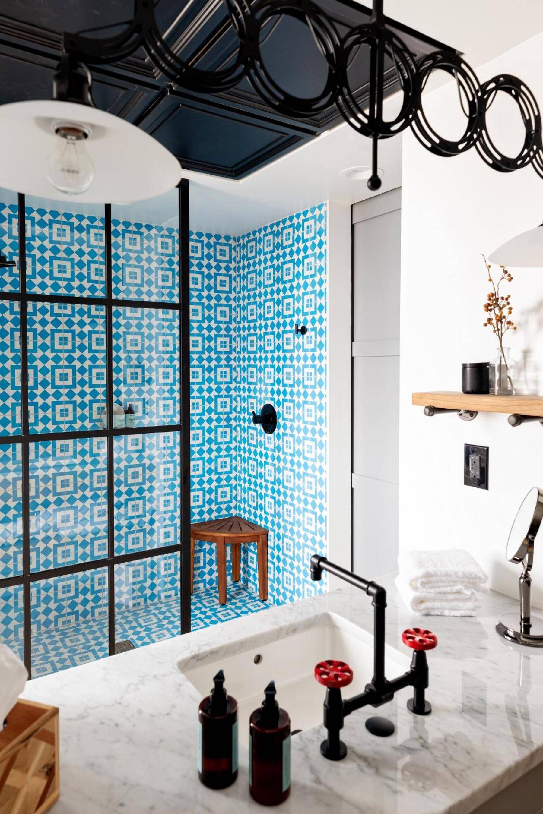 Geometric blue tiles create a bold Mediterranean backdrop in this striking bathroom, where industrial black fixtures and marble counters blend heritage charm with modern sophistication.