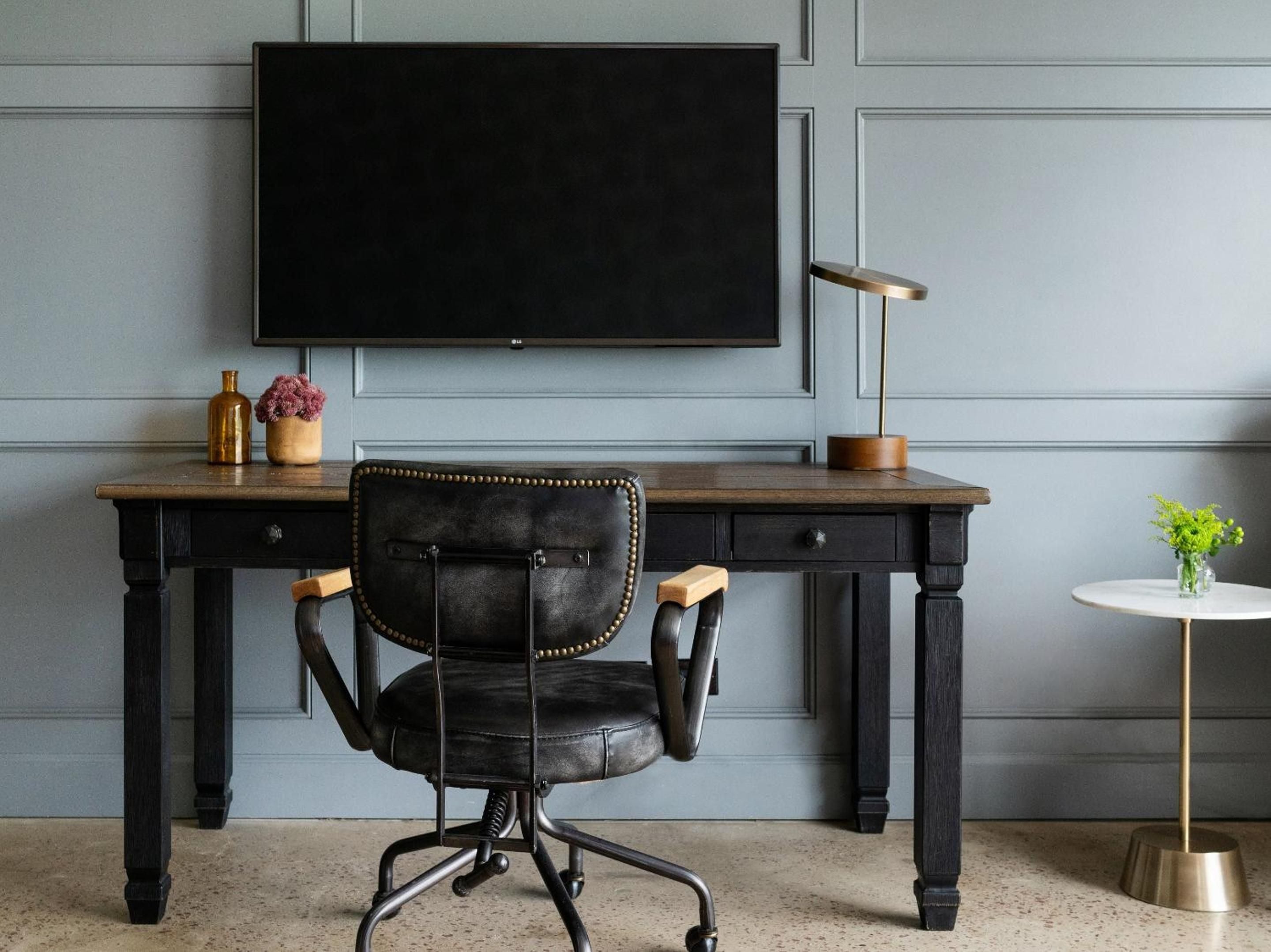 Charcoal leather and brass accents create an intimate workspace where industrial Memphis meets refined comfort, anchored by rich wood tones and thoughtful lighting.