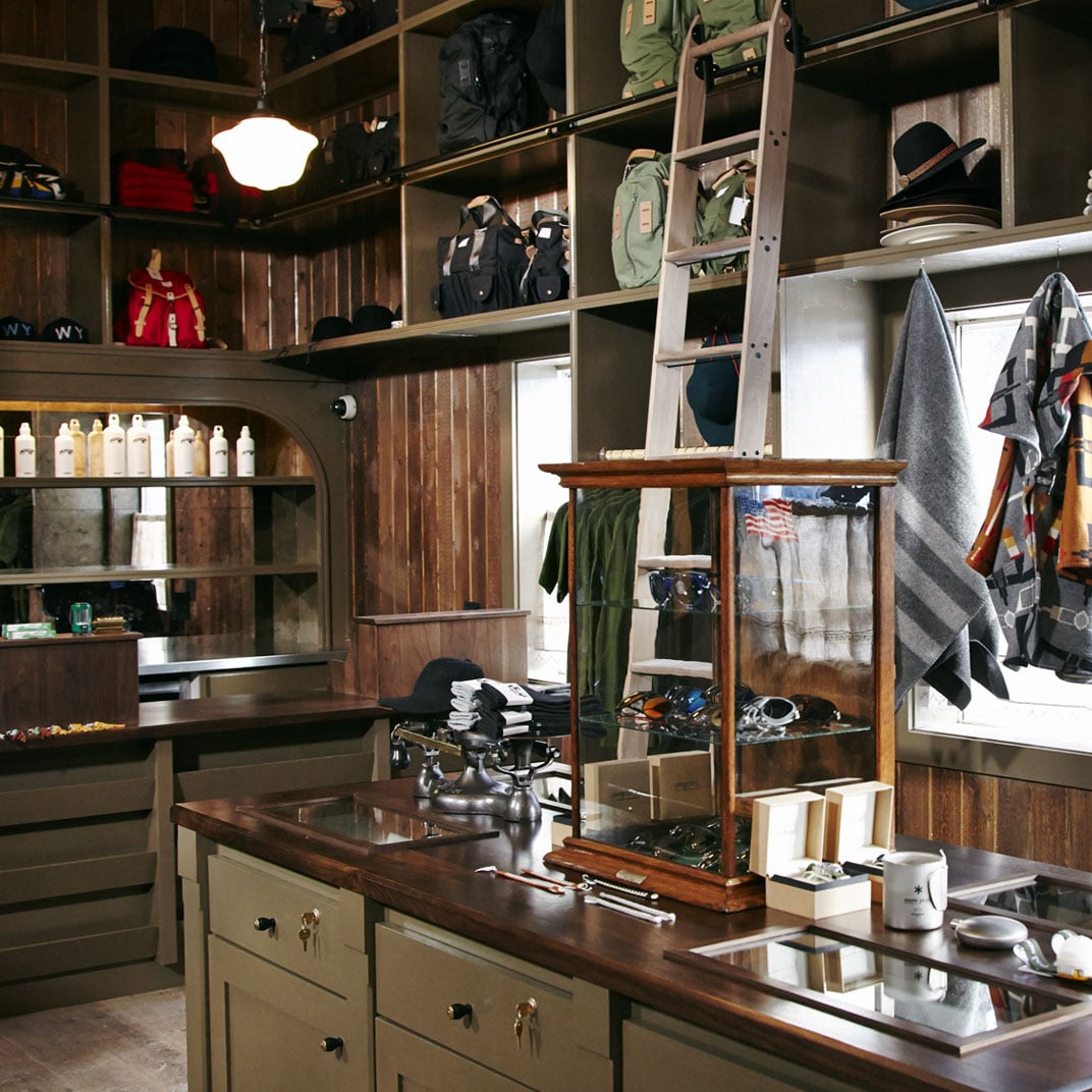 Raw wood shelving displays curated outdoor gear while vintage bottles and gleaming tools create an apothecary-meets-adventure aesthetic in this thoughtfully designed retail corner.