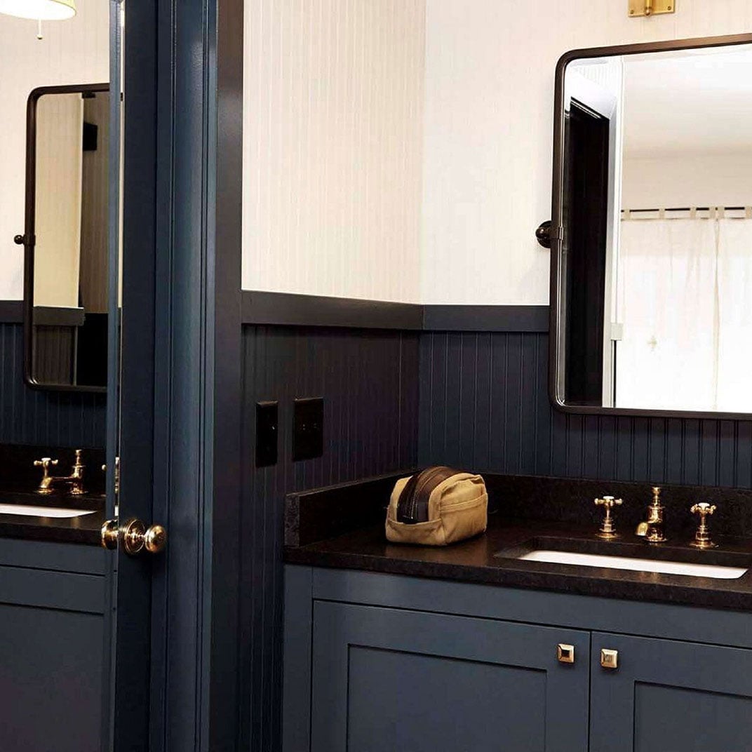 Navy blue cabinetry and brass fixtures create a sophisticated maritime aesthetic in the dual-vanity bathroom, where beadboard wainscoting meets modern luxury.