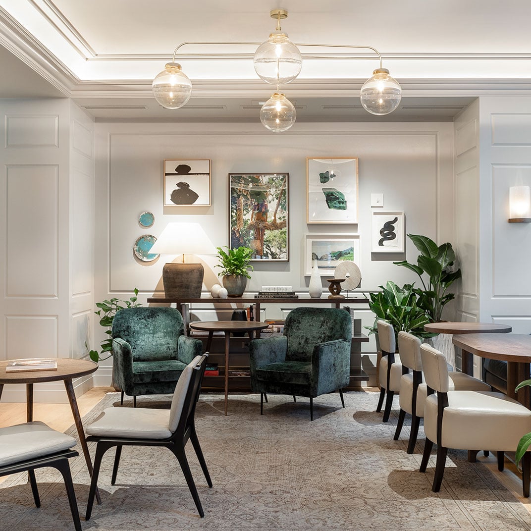 Globe pendant lights cast a warm glow over emerald velvet armchairs and curated artwork, creating an intimate reading nook within Woodlark's sophisticated common spaces.