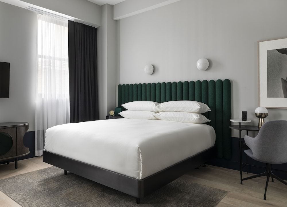 Emerald velvet headboard channels Art Deco glamour while natural light filters through sheer curtains, creating an intimate sanctuary above polished hardwood floors.