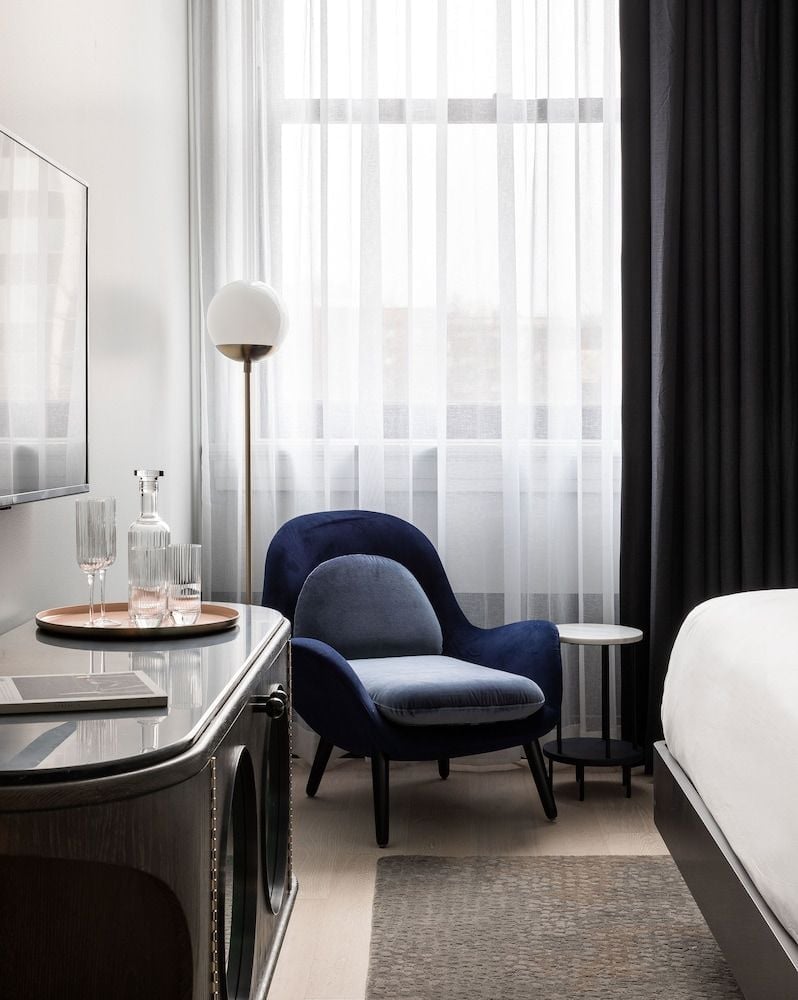 Navy velvet curves meet sleek surfaces in this thoughtfully appointed guest room, where crystal decanters catch afternoon light streaming through pristine white curtains.